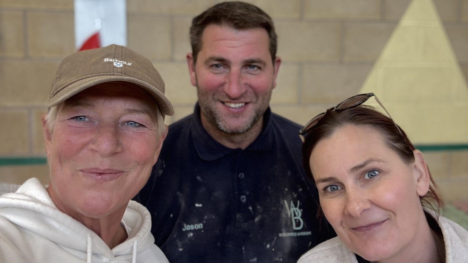 Paula Conde-Sharpe, Jason Sharpe and Anne Ahktar, in a room, looking at the camera. Paula has a beige cap on, and white top, Jason, a paint splattered top and Anne has long dark hair with glasses on her head.