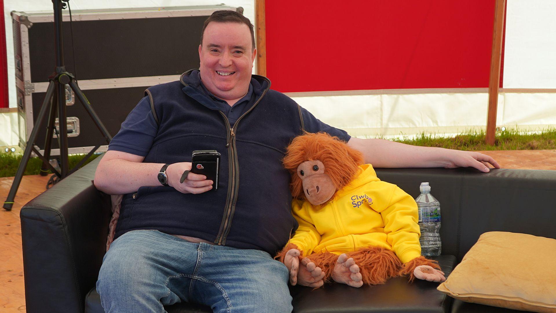 Gareth yr orangutan yn eistedd ar gadair gydag oedolyn