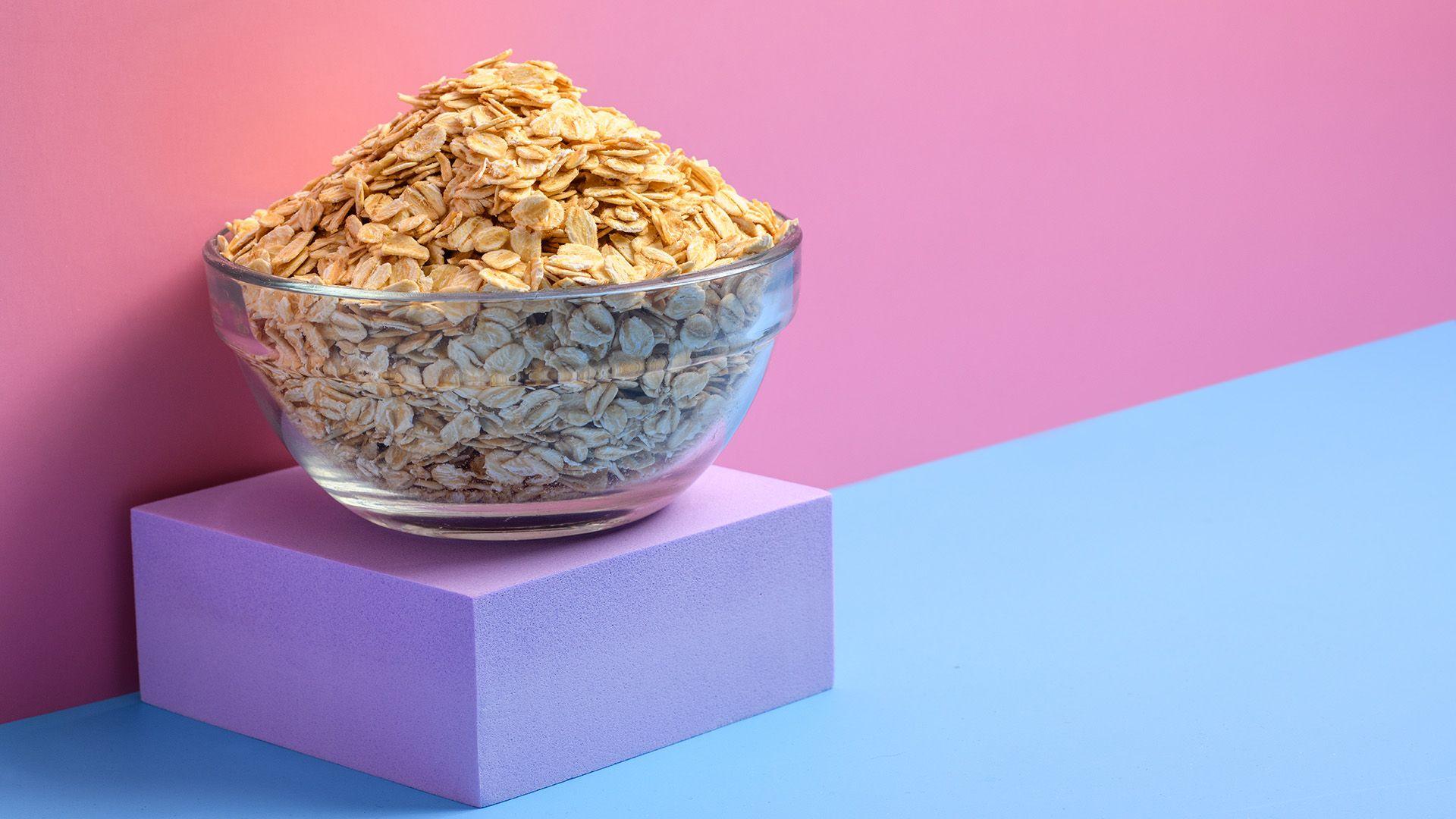 A bowl of rolled oats on a purple block with a pink and blue background