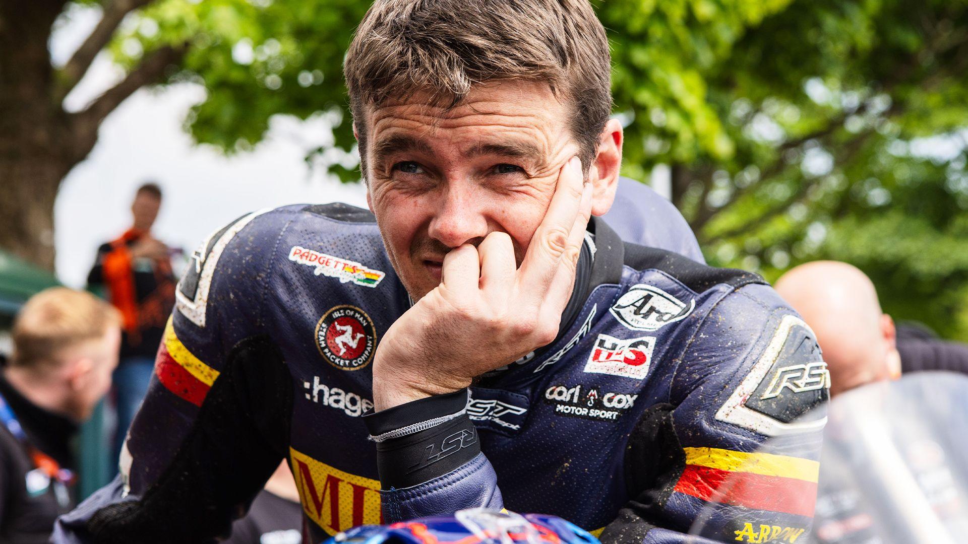 A man in motorbike leathers with his chin resting on his hand