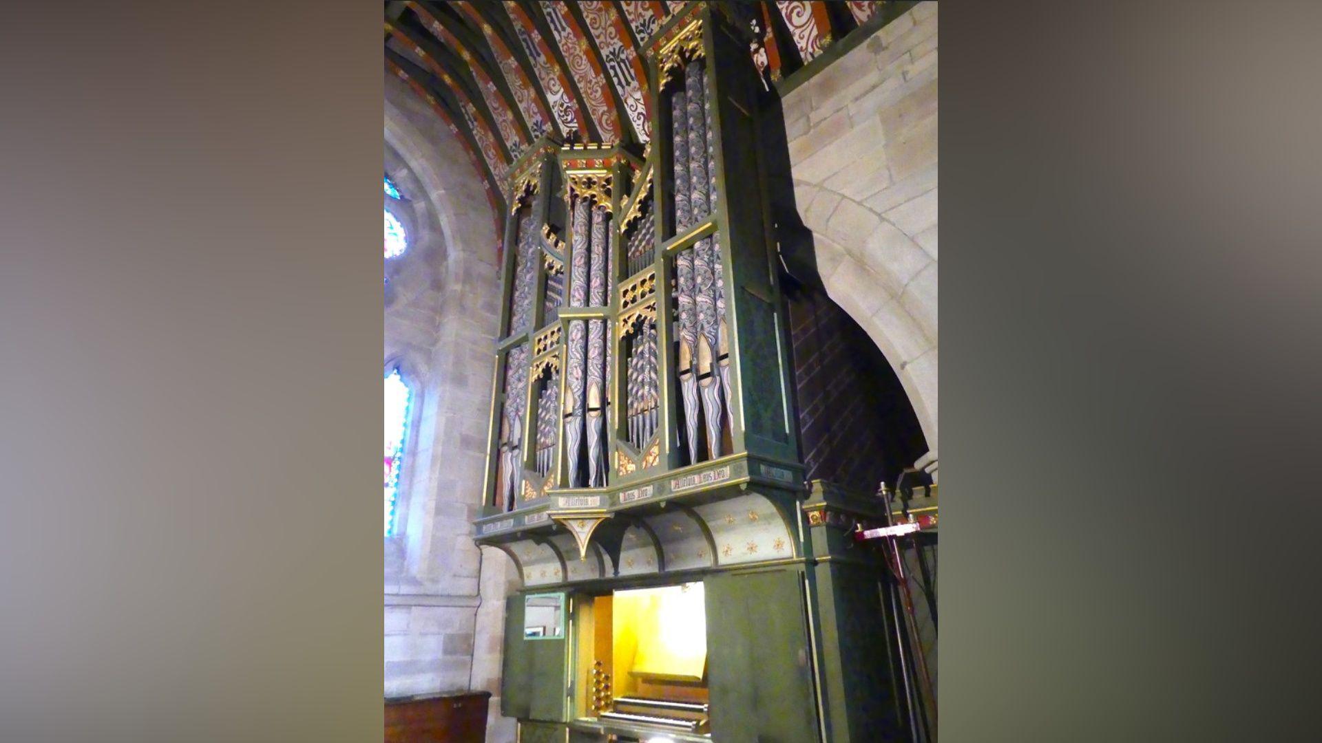 A 19th Century organ with green casing and gold and black pipework inside a stone Hanbury church.