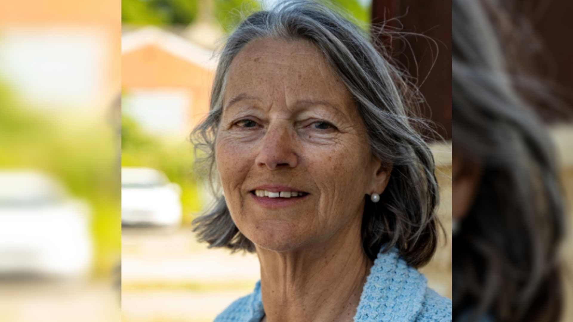 Jennifer Morisetti  smiling at the camera has short grey hair and is wear pearl earrings and a blue jumper.