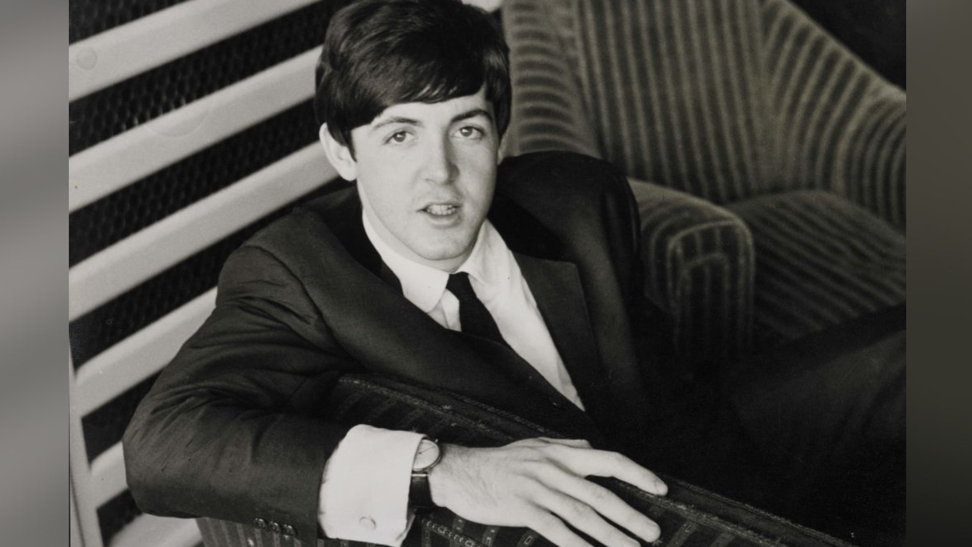 A black and white photo of a man in a suit, sitting on a couch.