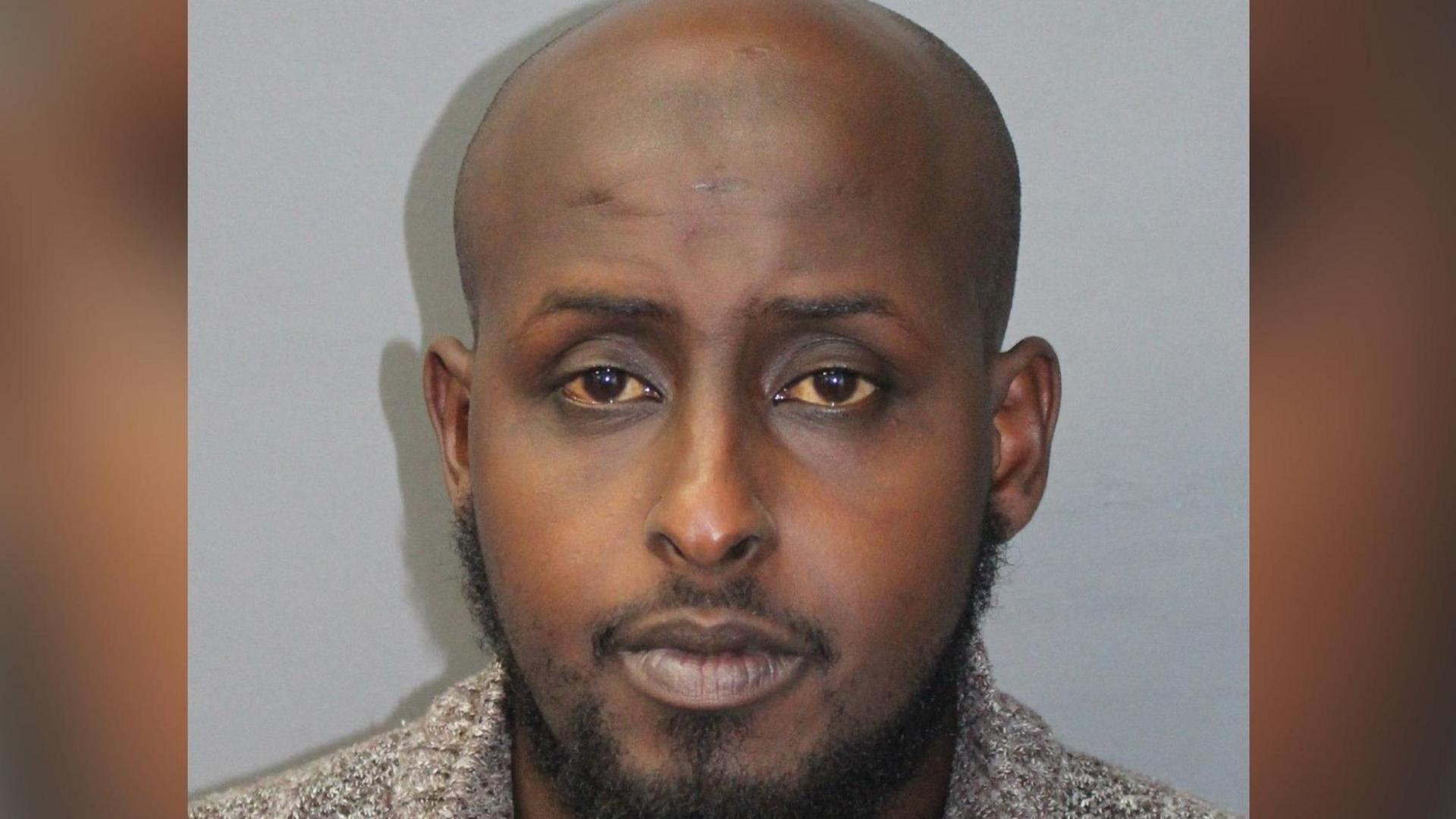 Police mugshot image of Mohamed Iidow, a black man with a bald head and facial hair