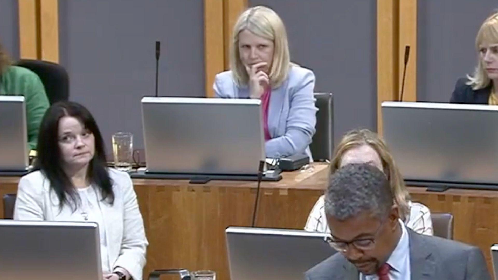 Hannah Blythyn watches from the back of the Senedd and Vaughan Gething speaks in front of her 