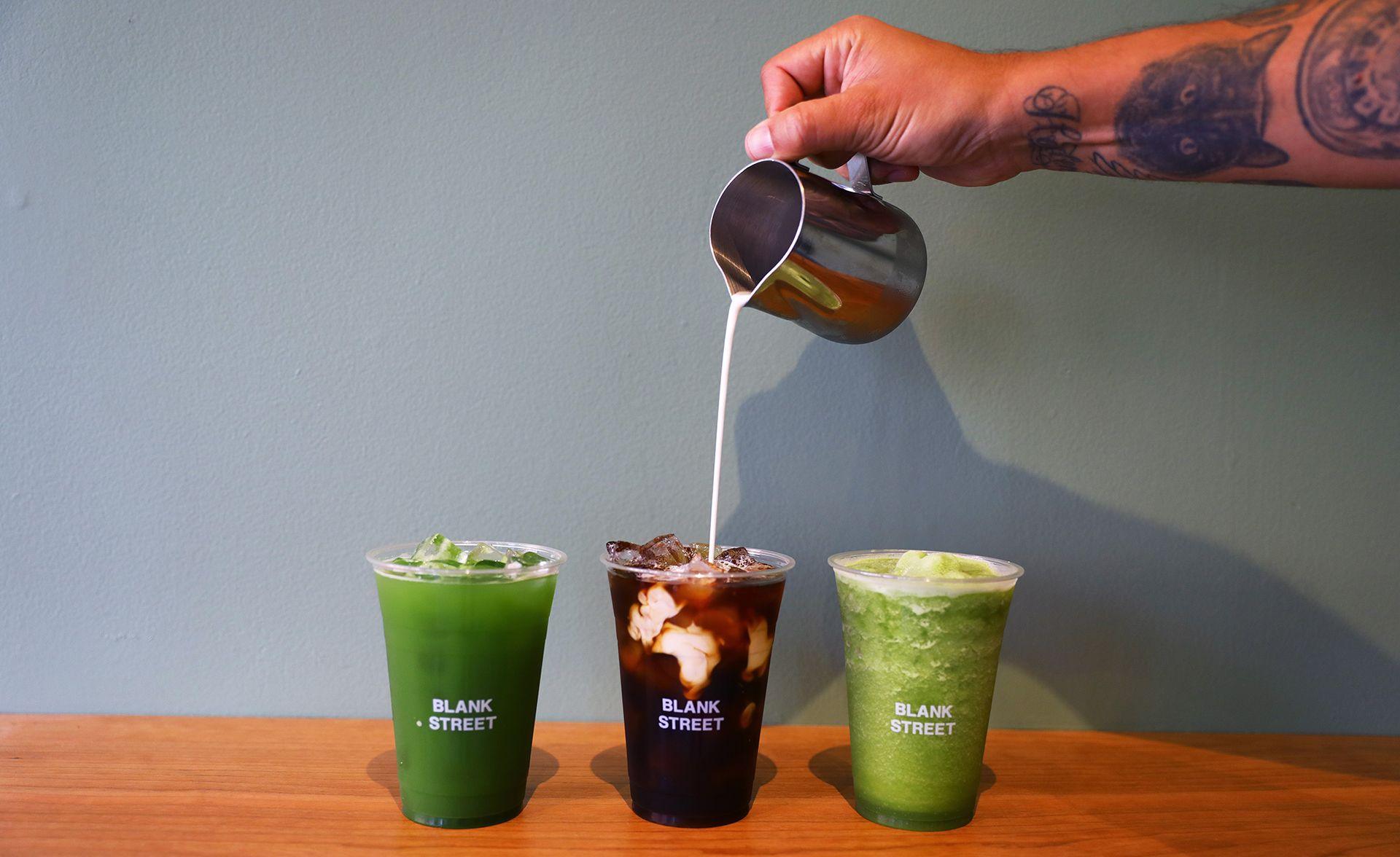Specialty beverages in clear plastic cups with Blank Street written on them in white, from left, a green Iced Matcha Tea, a brown Cold Brew Coffee with swirls of cream and a lighter green Blended Lemon Matcha