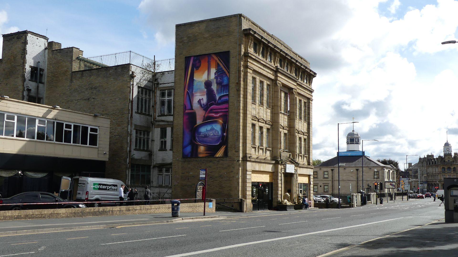 Colourful vertical mural on the side of a four-storey building which looks old with ornate stone work.