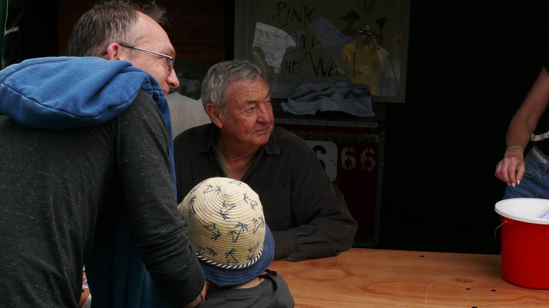 Nick Mason sits at a bench. A man and a young boy stand in front of him