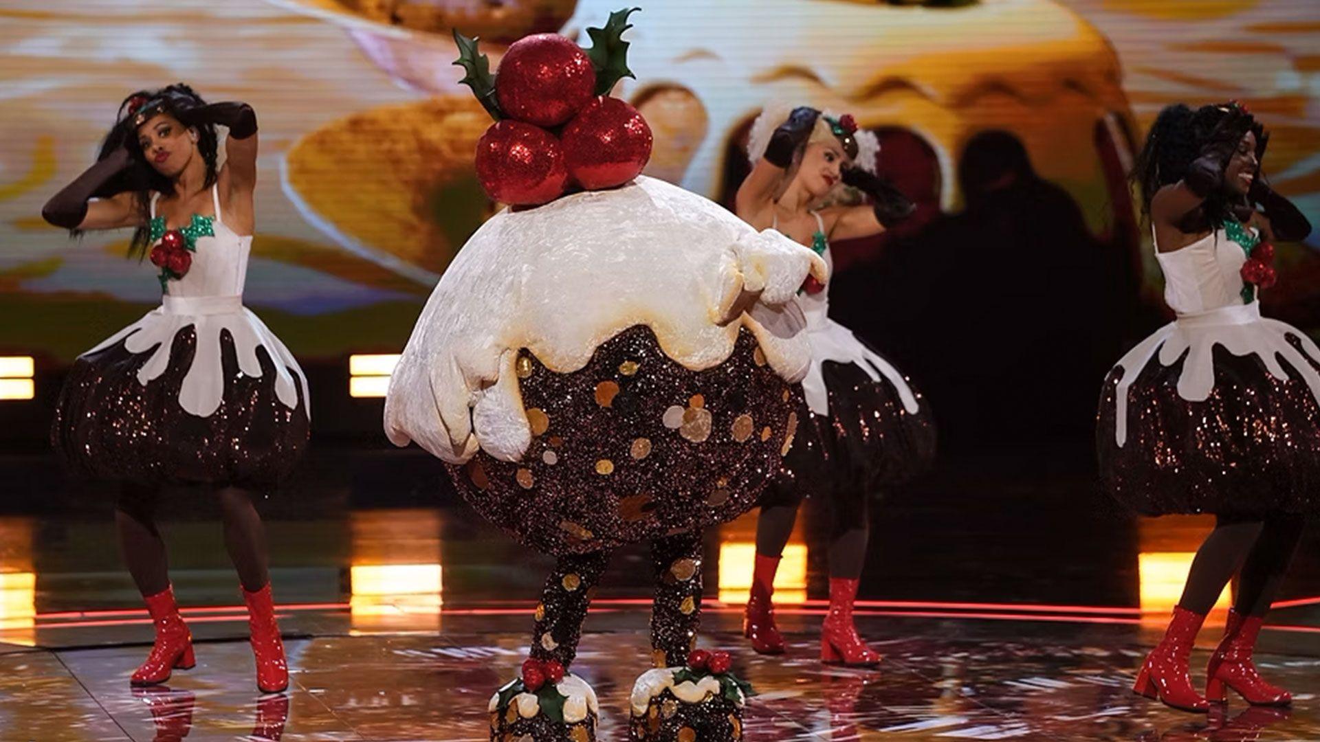 A singer dressed as a large Christmas pudding dances on stage