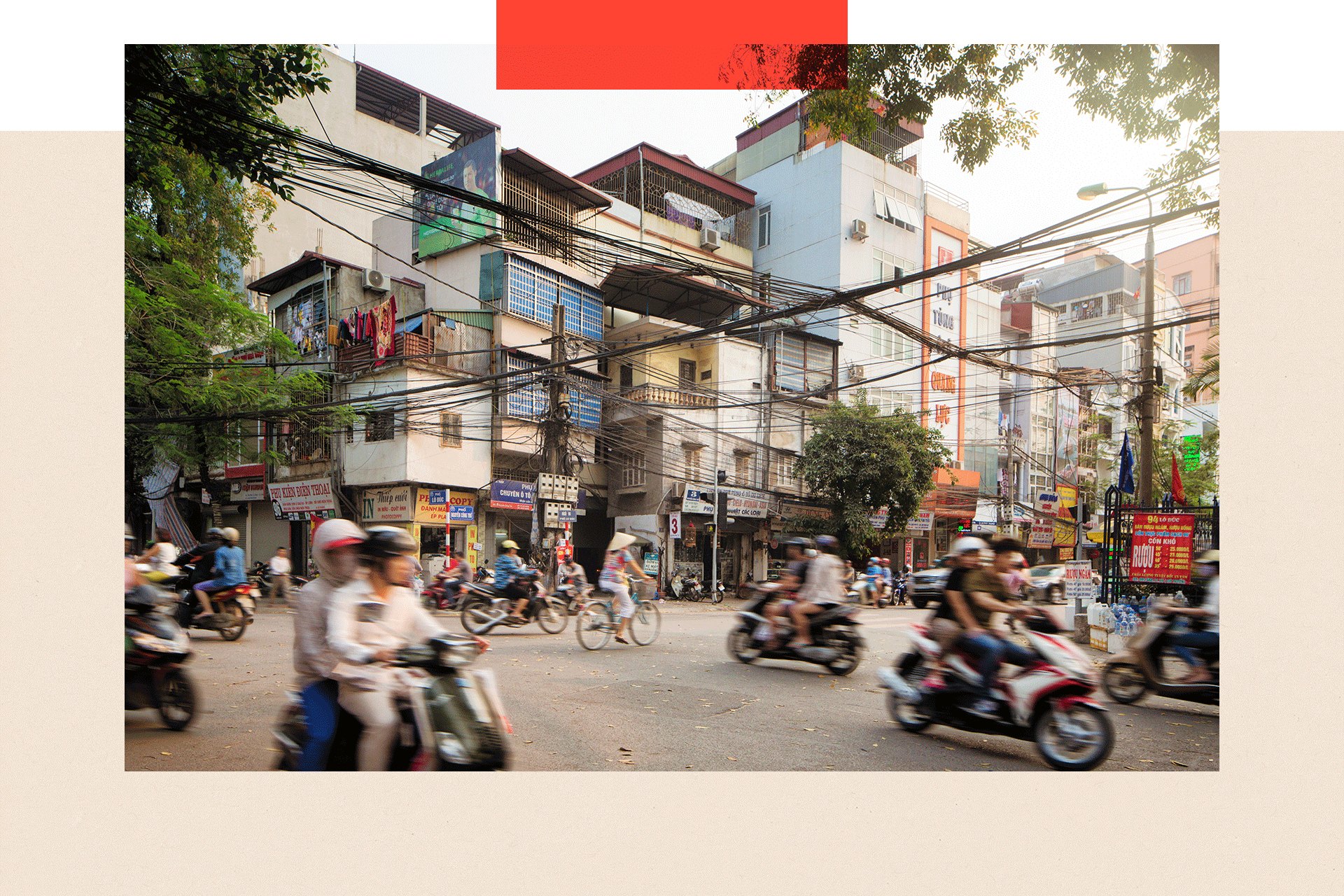 Morning traffic on Lo Duc Street in Hanoi, Vietnam on a warm spring day. People are commuting on bikes and motorbikes, or walking and shopping. Apartment buildings are rising above the street behind electric cables.
