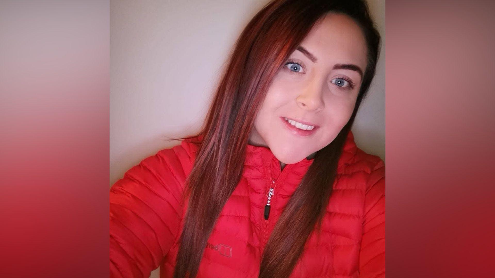 The image is a selfie of Lauren Marshall. She's dressed in a red padded zip up jacket and is smiling at the camera. Her hair is dark and long.