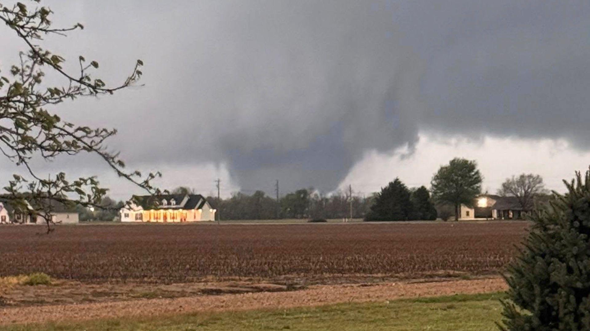 Large tornado on the ground behind field and houses