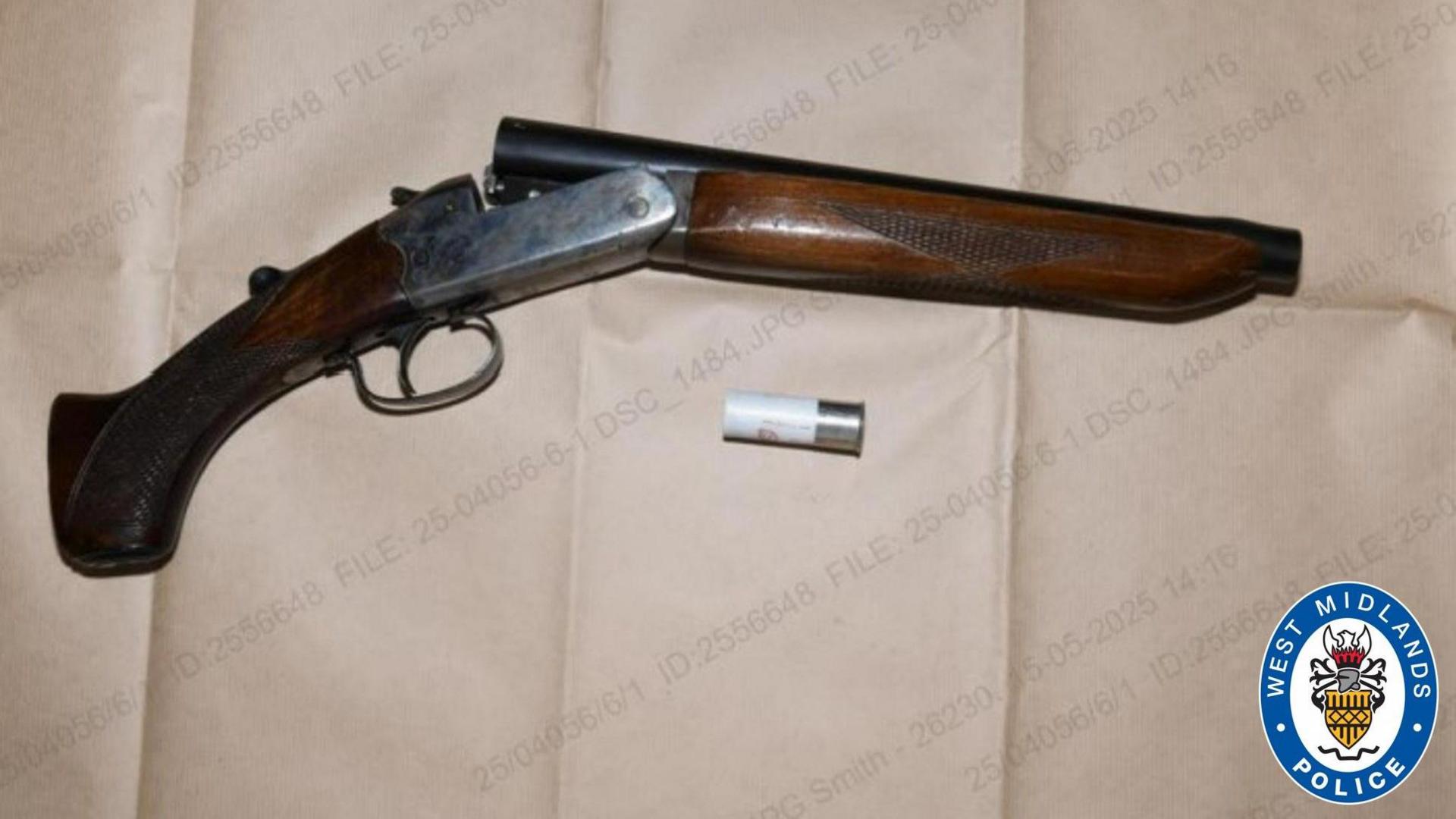 A shortened brown shotgun with a cartridge on a plain background. The image has the West Midlands Police logo in the bottom right corner, which is blue and white with a yellow, red, white and black crest.