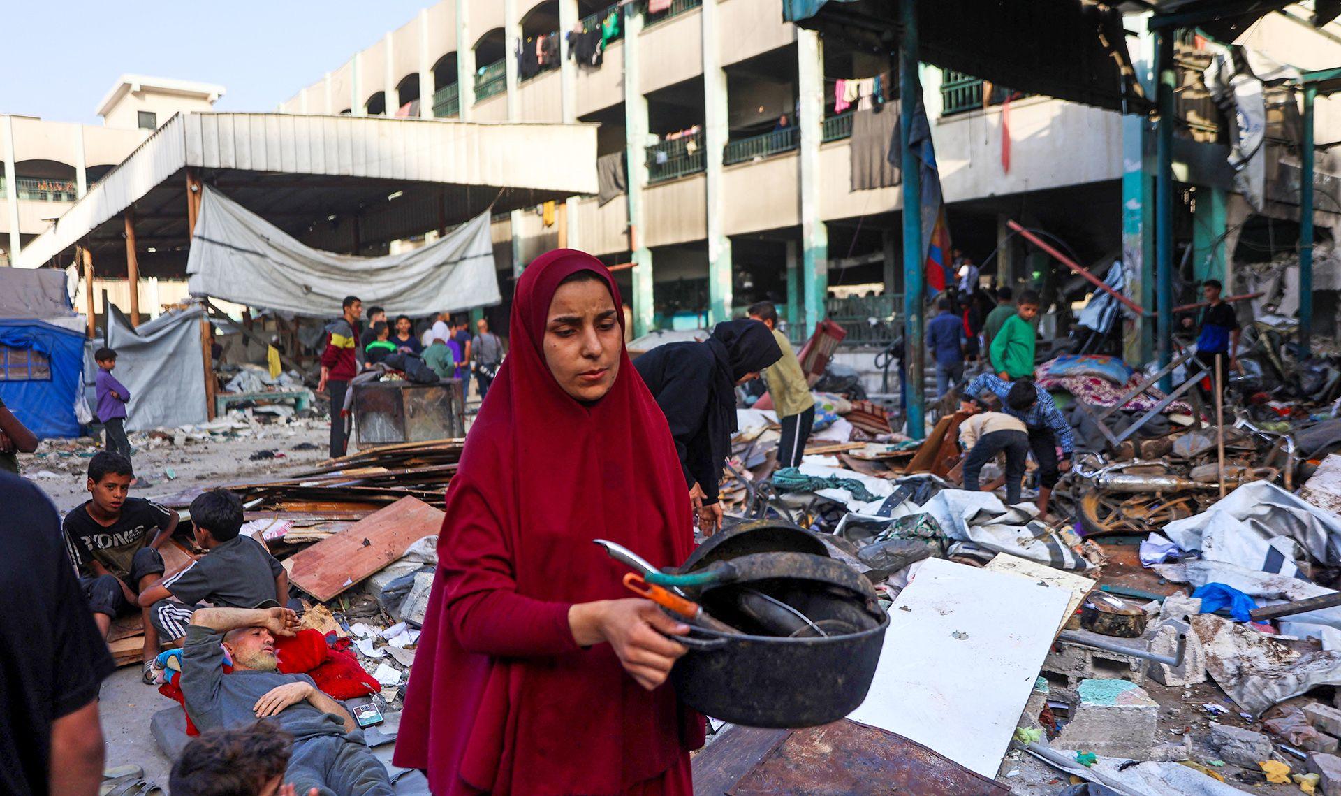 A woman collects salvagable goods with rubble and materials all around her in the middle of the Fahmi Al-Jargawi School courtyard on Monday