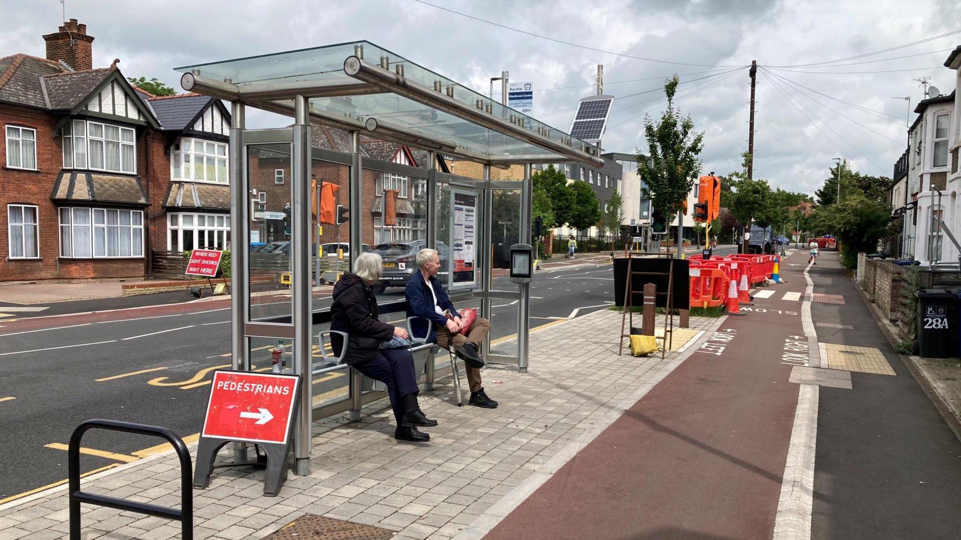 People waiting at a bus stop in Cambridge. There are roadworks taking place.