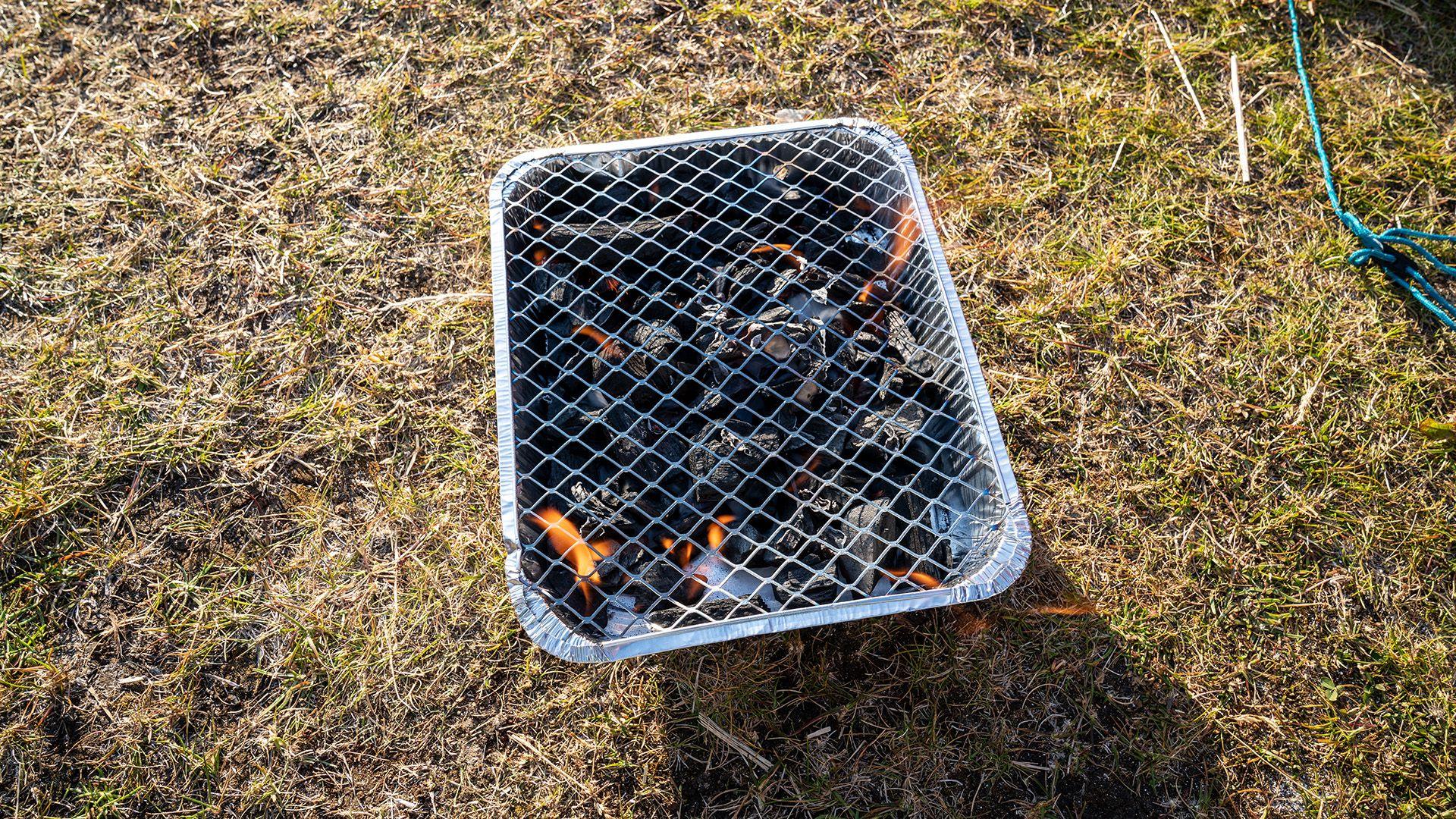 A lit disposable barbecue sits on dry grass