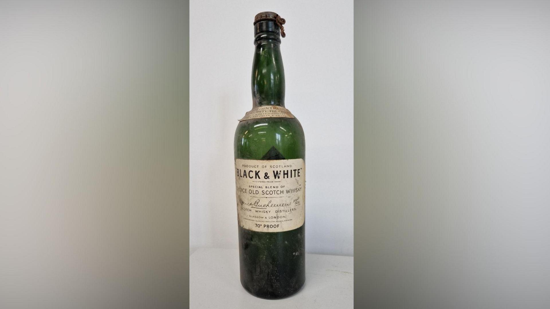 A composite image showing the empty Black & White Scotch whisky bottle, which is green glass with an off white label.
