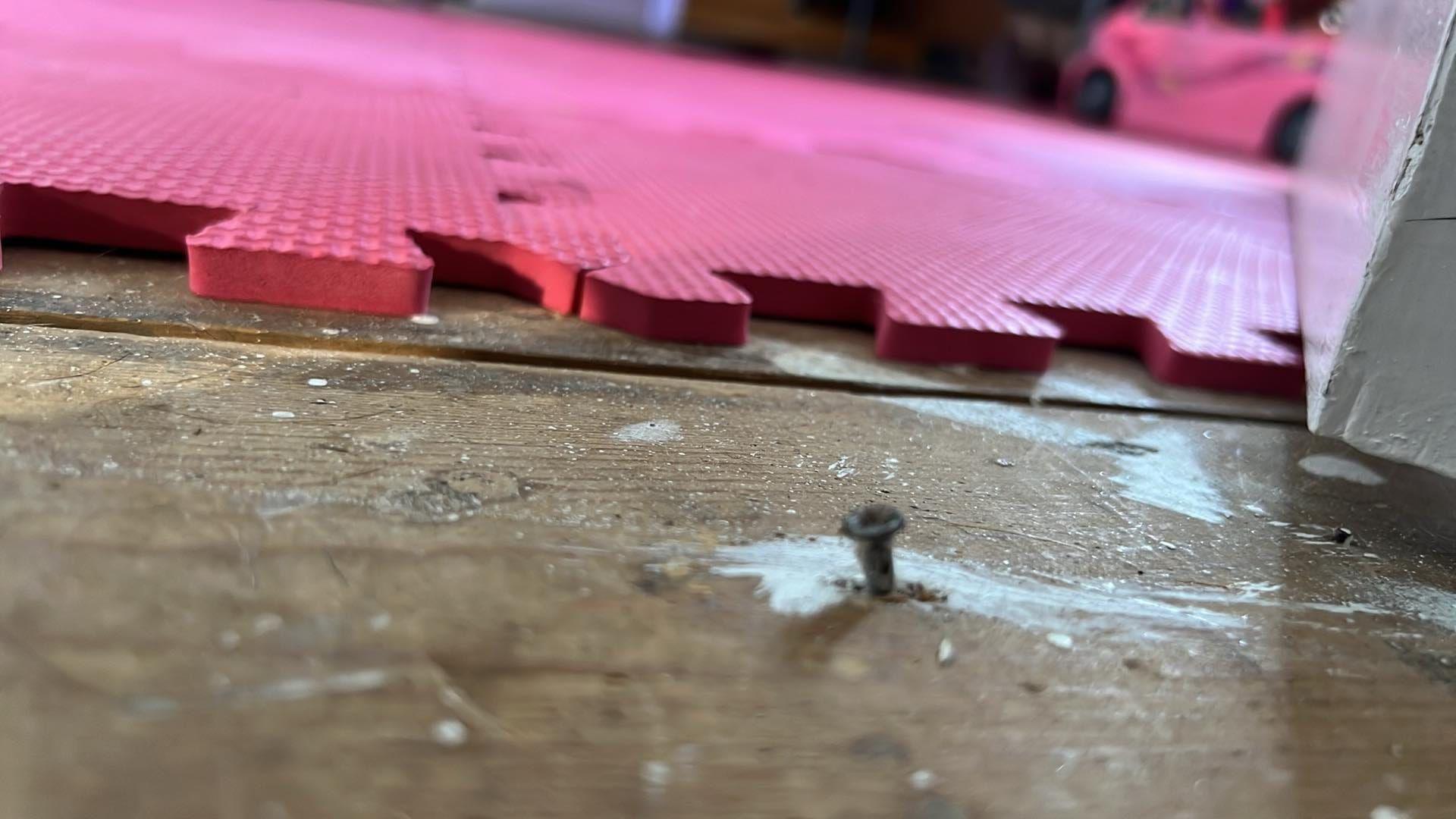 A nail sticks up from the floor with a children's play area in the background