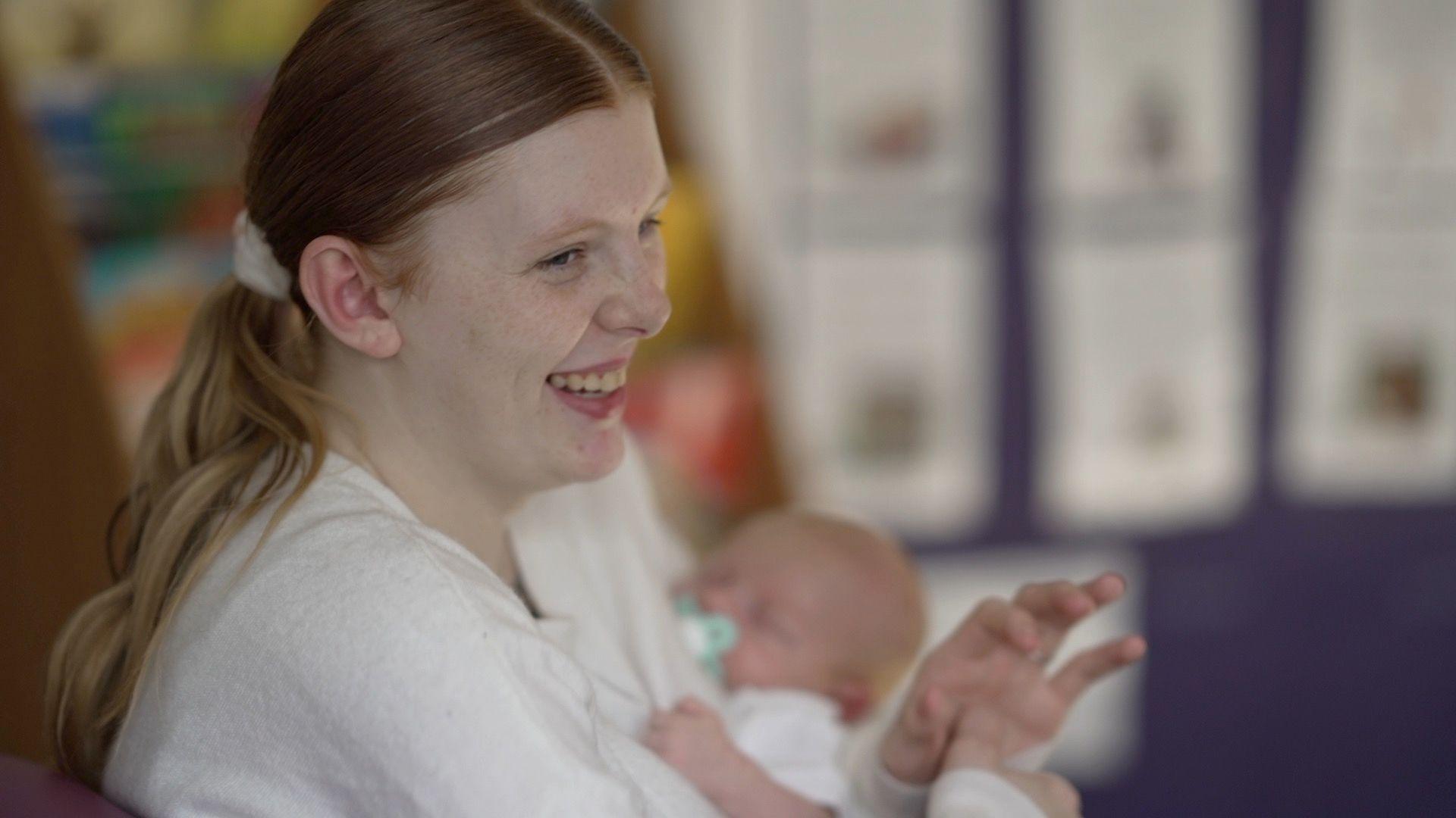 A young mum, cuddling her baby laughs 