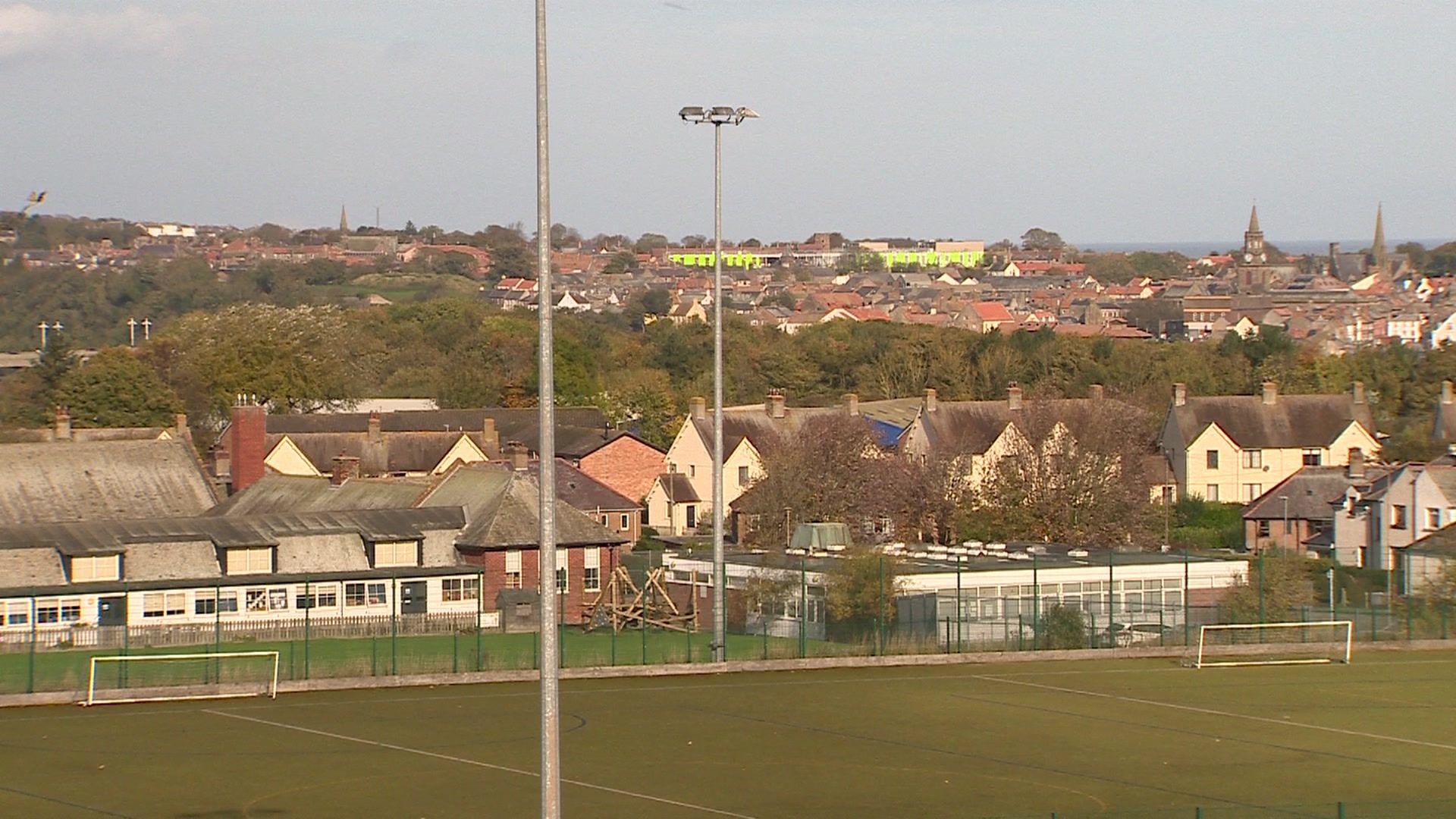 Berwick Middle school covers the middle section of the image with its one storey buildings and some temporary classrooms. In the foreground you can see the school's playing fields and behind the town and some trees 