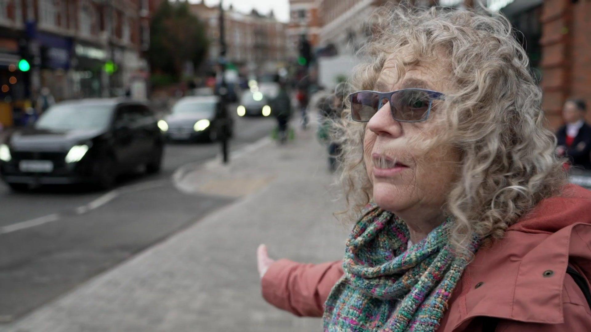A woman looking cross and gesticulating at a pavement.