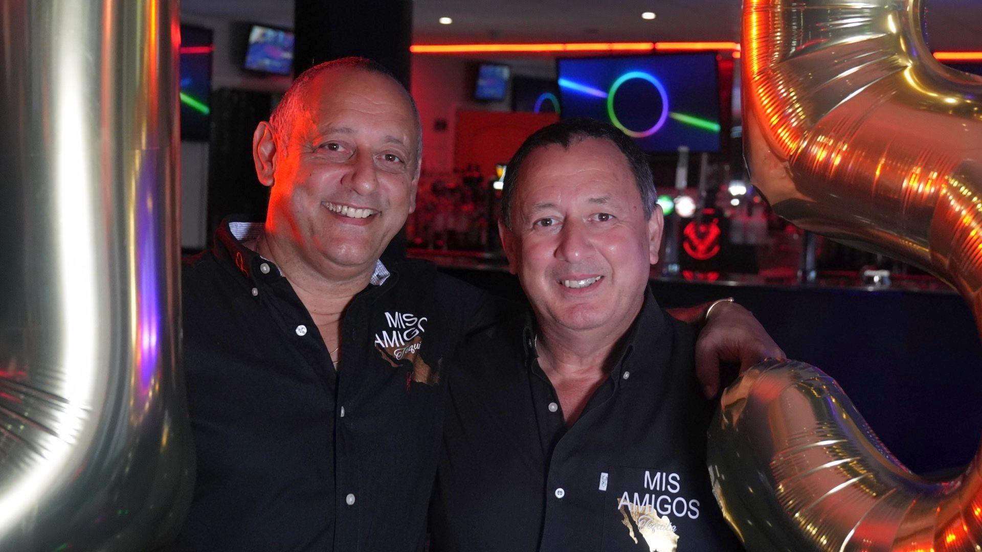 The Duke brothers, who are both wearing black shirts, stand between two large balloons in a nightclub.