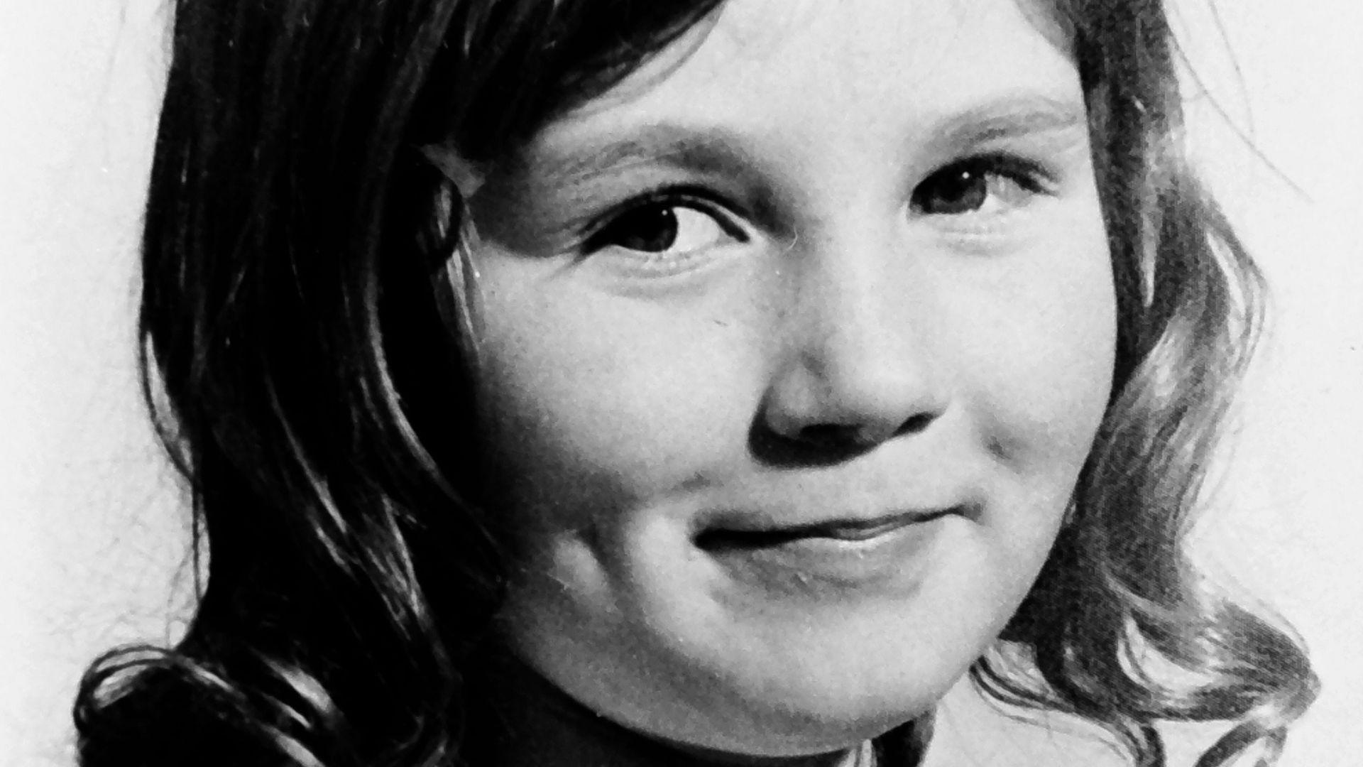 A black and white photograph of a young girl with dark curly shoulder length hair. 