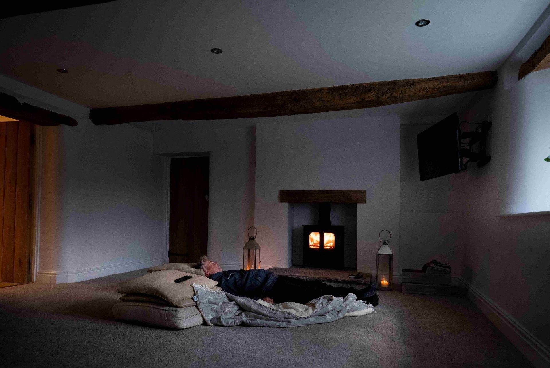 Andrew Jackson lying down on some blankets and cushions in an empty room, with a lit wood burner 