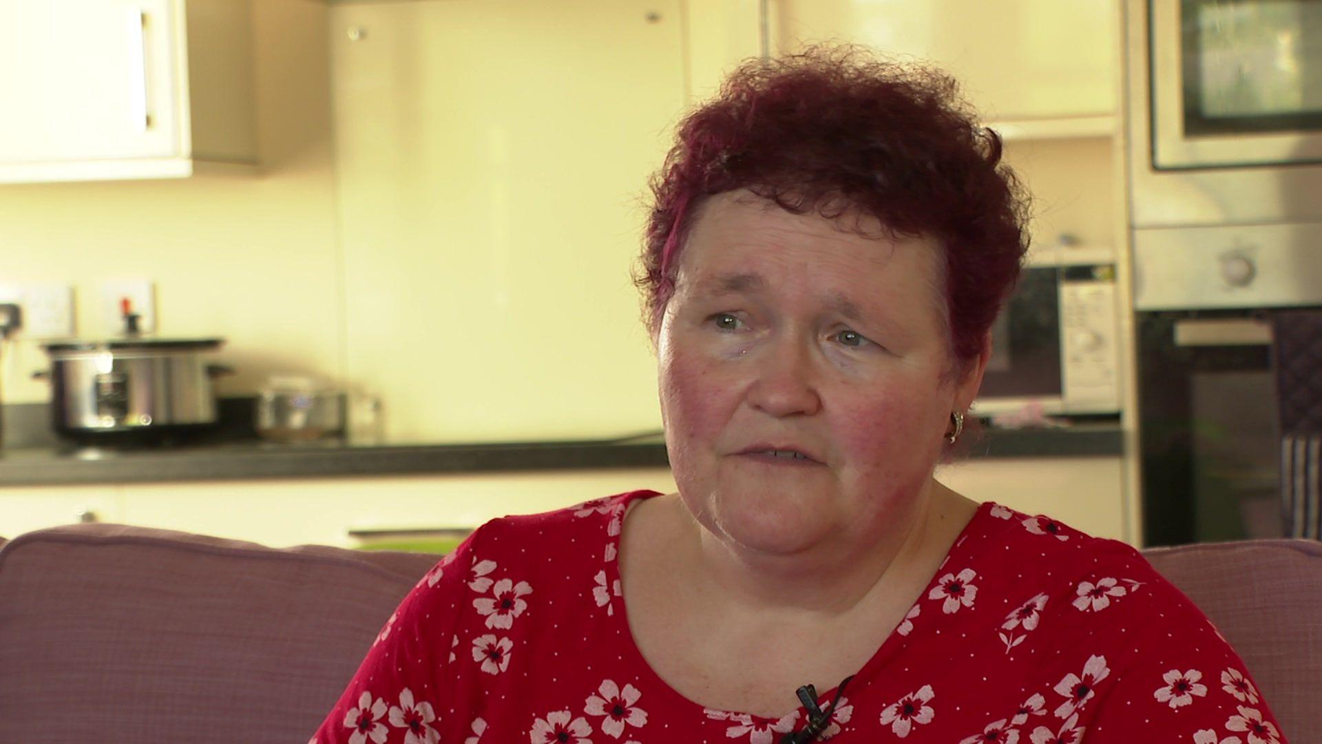 Claire Throssell sits on a sofa wearing a red top dotted with white flowers.