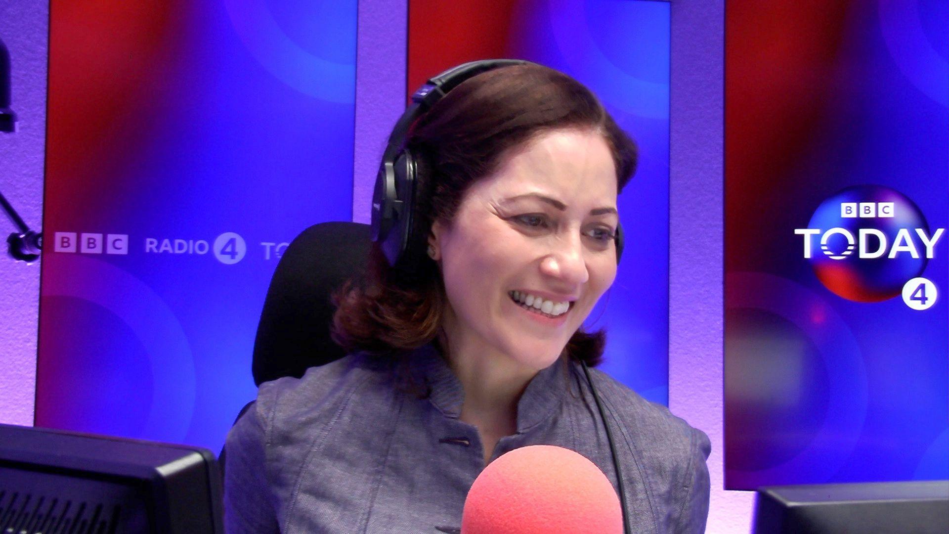 Mishal Husain wearing headphones infront of a blue and red graphic with BBC Today 4 written on it in the Today programme studio