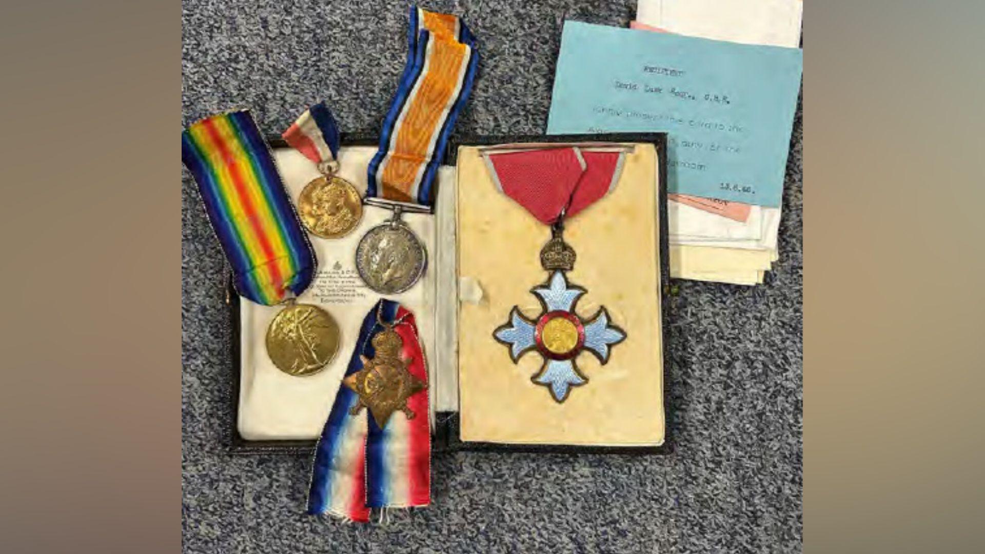 Several medals with ribbons attached including one in a box, lying on a carpet
