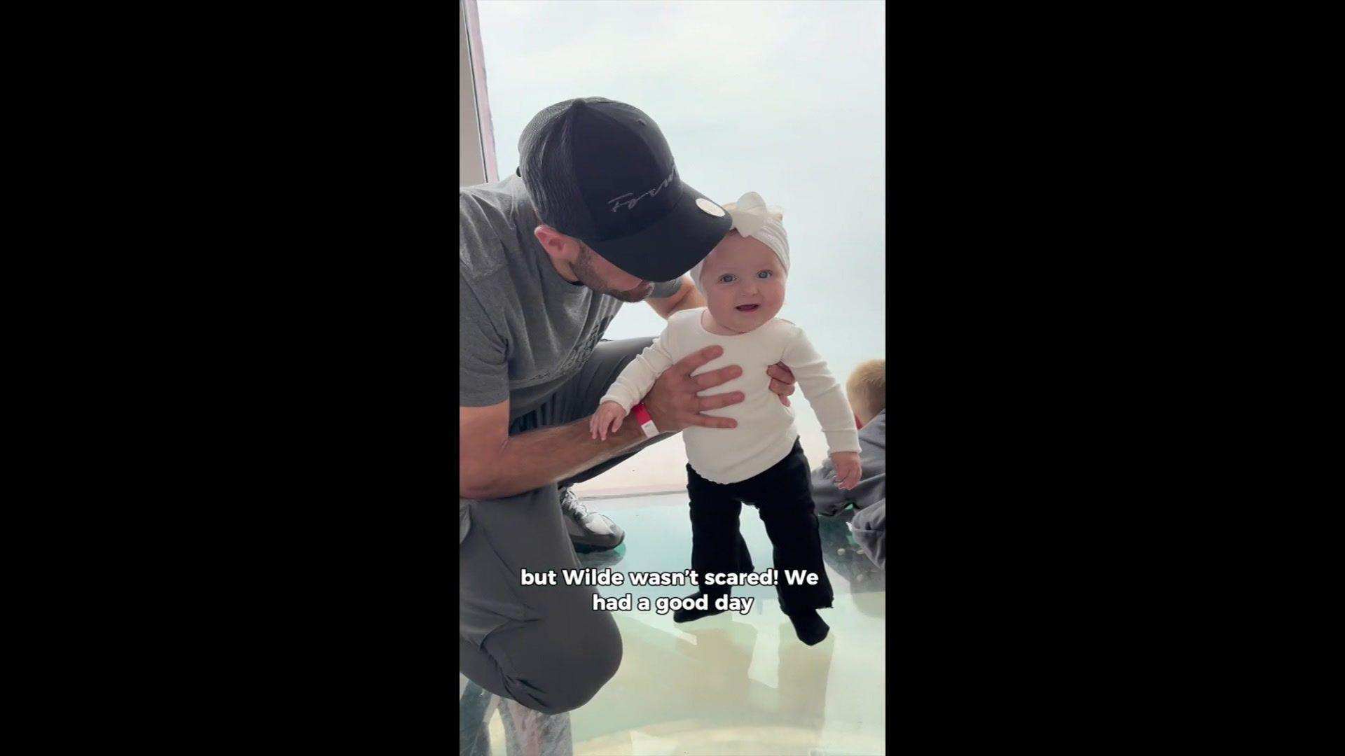 Man wearing a black cap holding a baby who is standing up and smiling at the camera