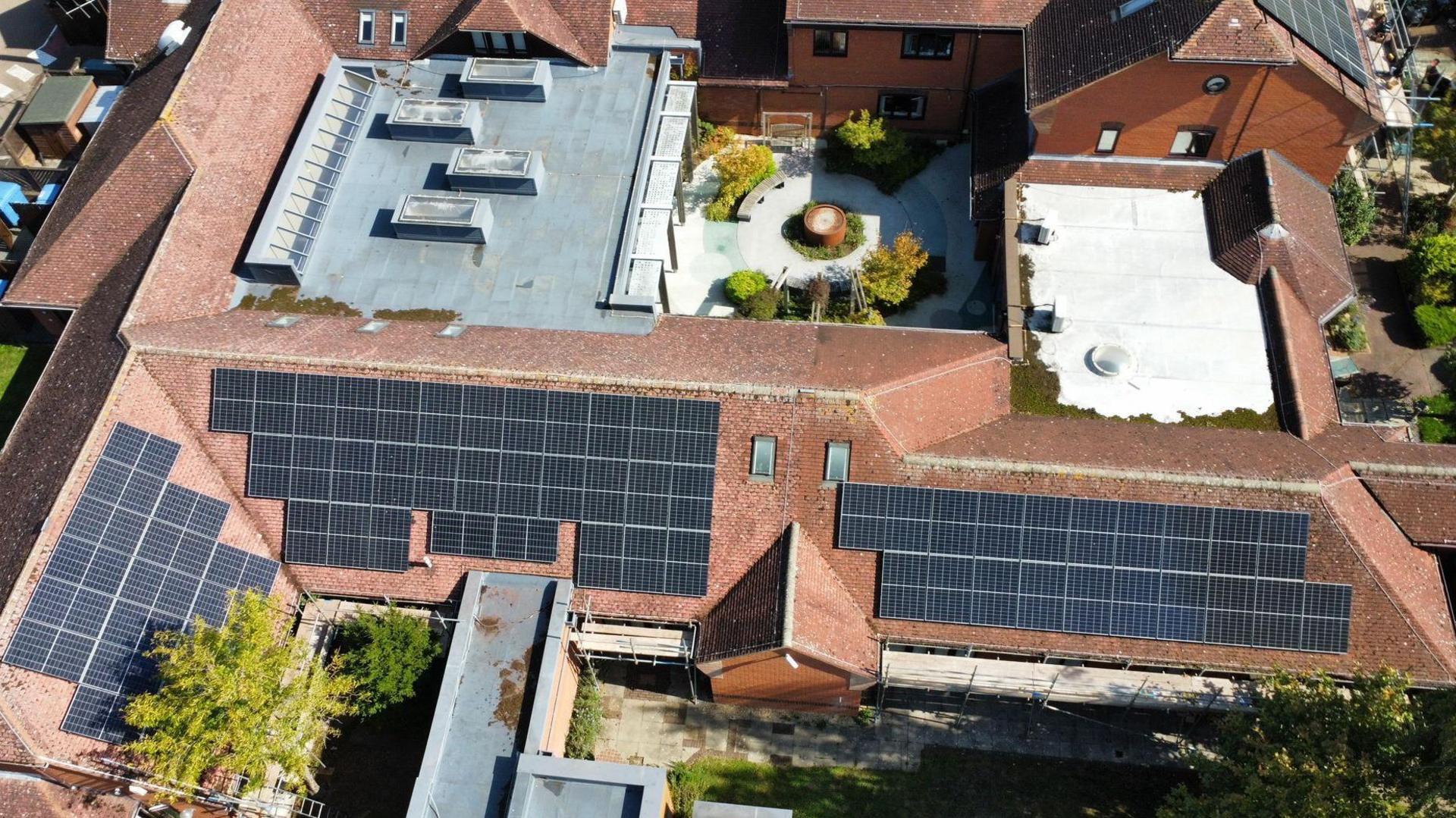 An aerial drone shot of the hospice roofs, which consist of several connected buildings. Four sections are covered in black solar panels. 