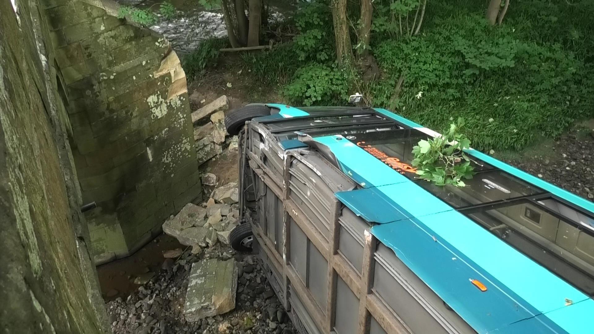 Single decker bus laid on its side next to the damaged bridge