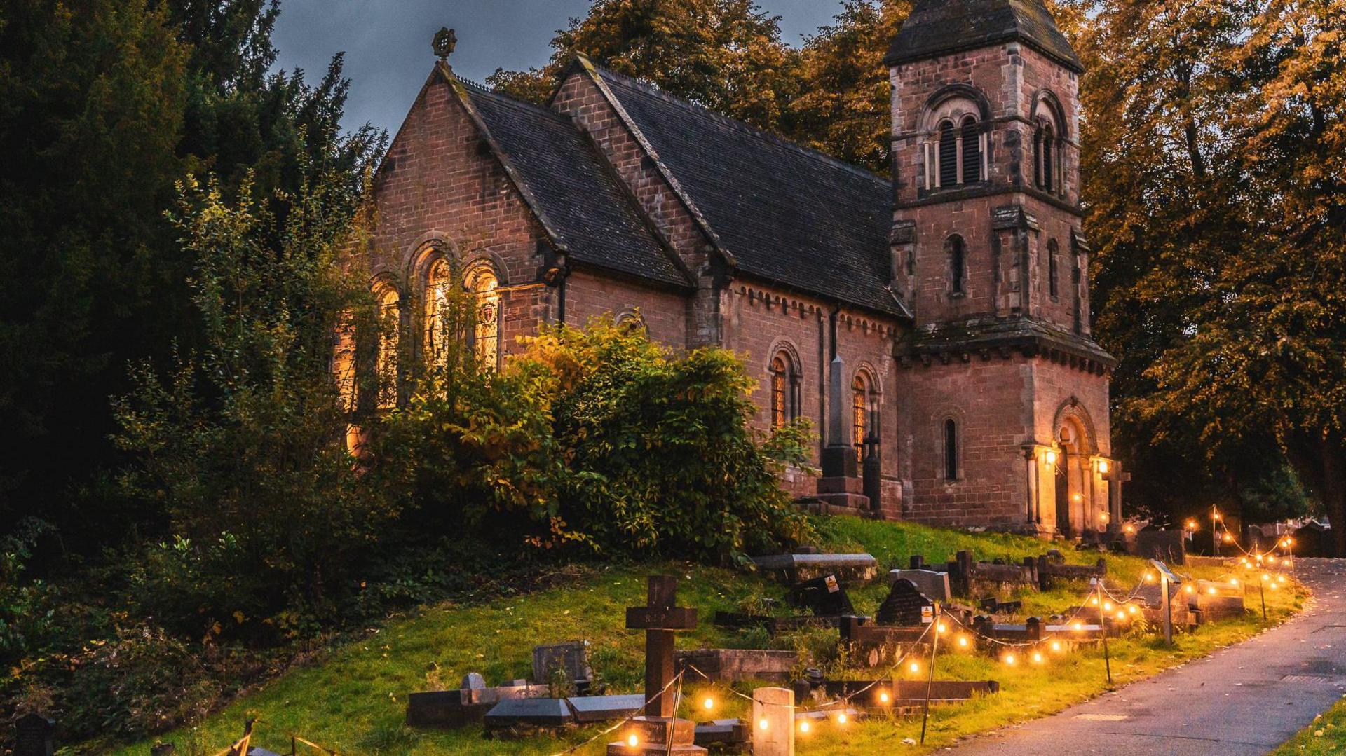 Night time picture showing the lanterns shining brightly at the edge of the footpath leading up to the church. 