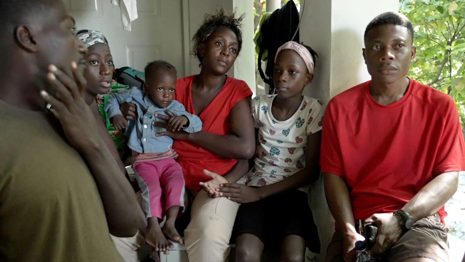 A woman sits with her child on her knee next to her other children