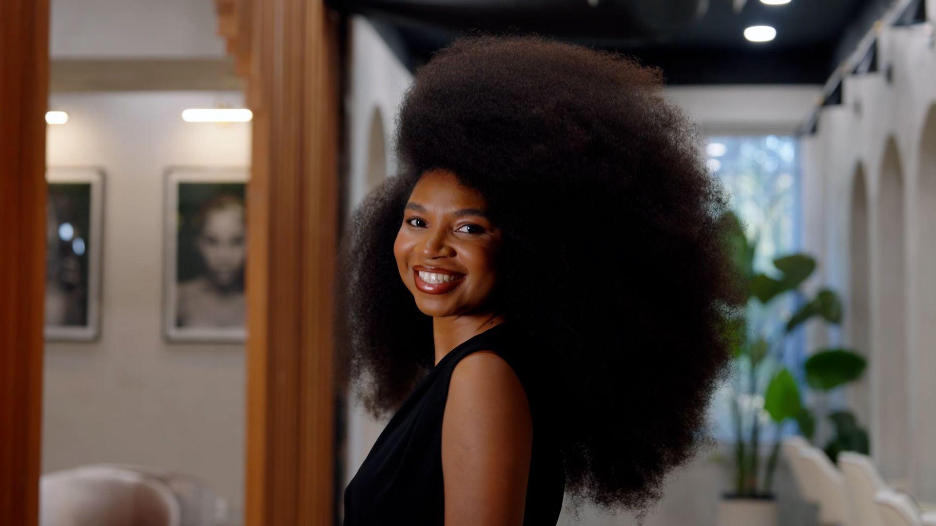 A woman with a large afro hairdo smiles at the camera
