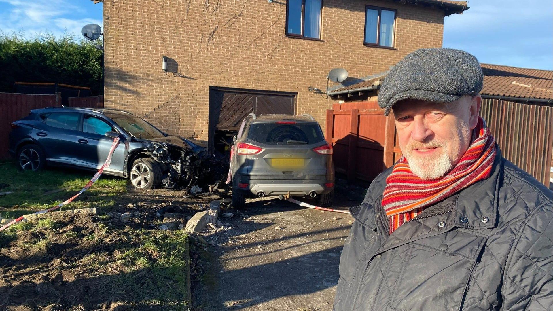 Dean Wilson looks at the camera in front of two damaged cars outside Calverton Miners Welfare