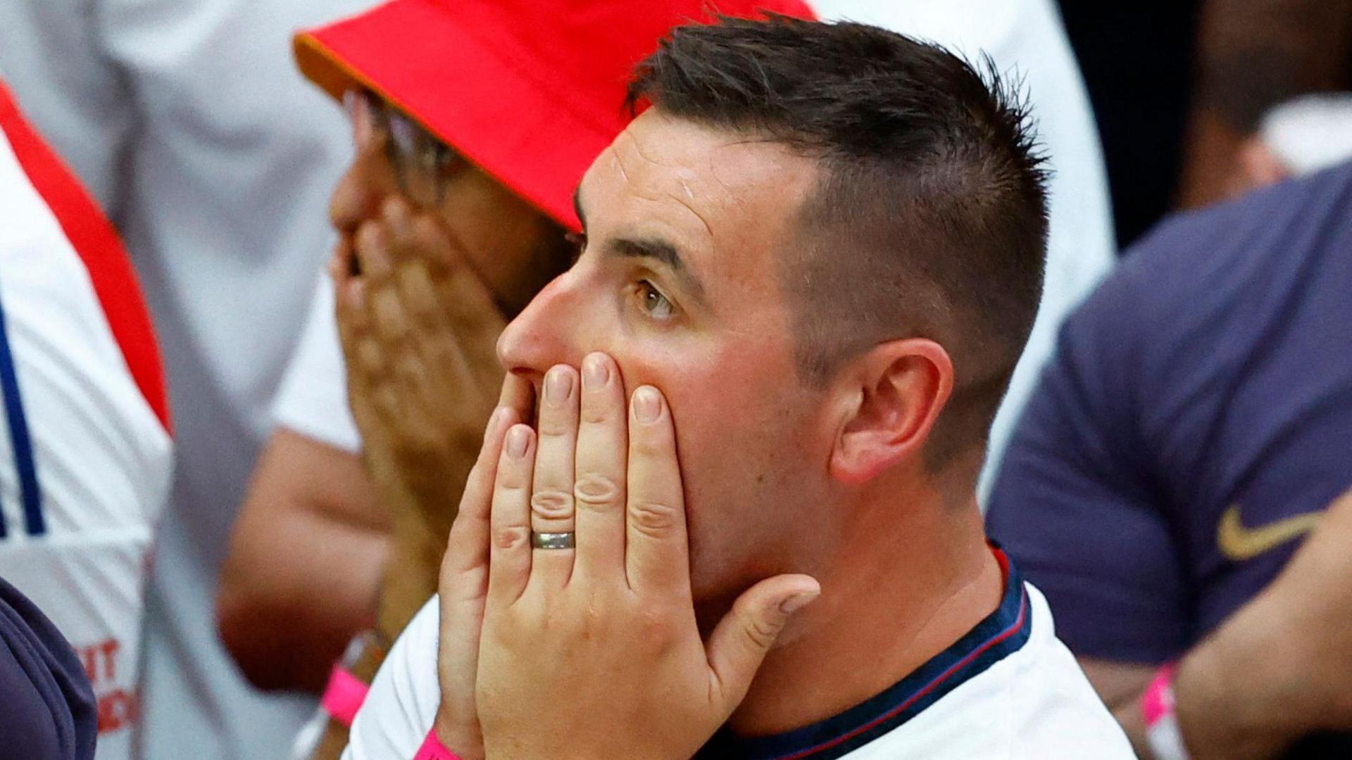 Man in a crowd puts his hands on his face as he watches on