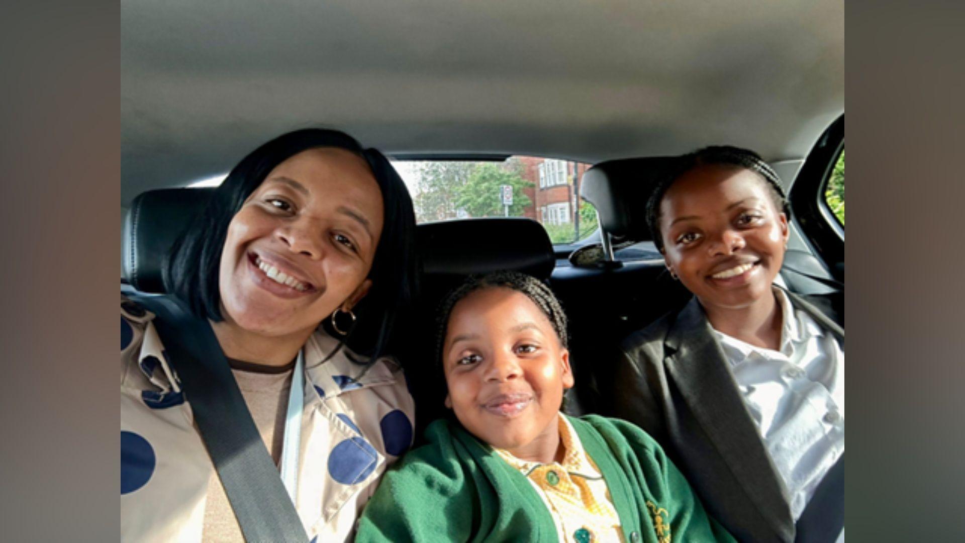 A mum in a car, alongside her two daughters. They are all smiling. 