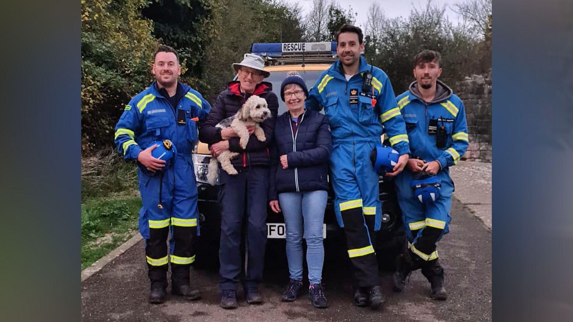 A couple holding a dog surrounded by a rescue team