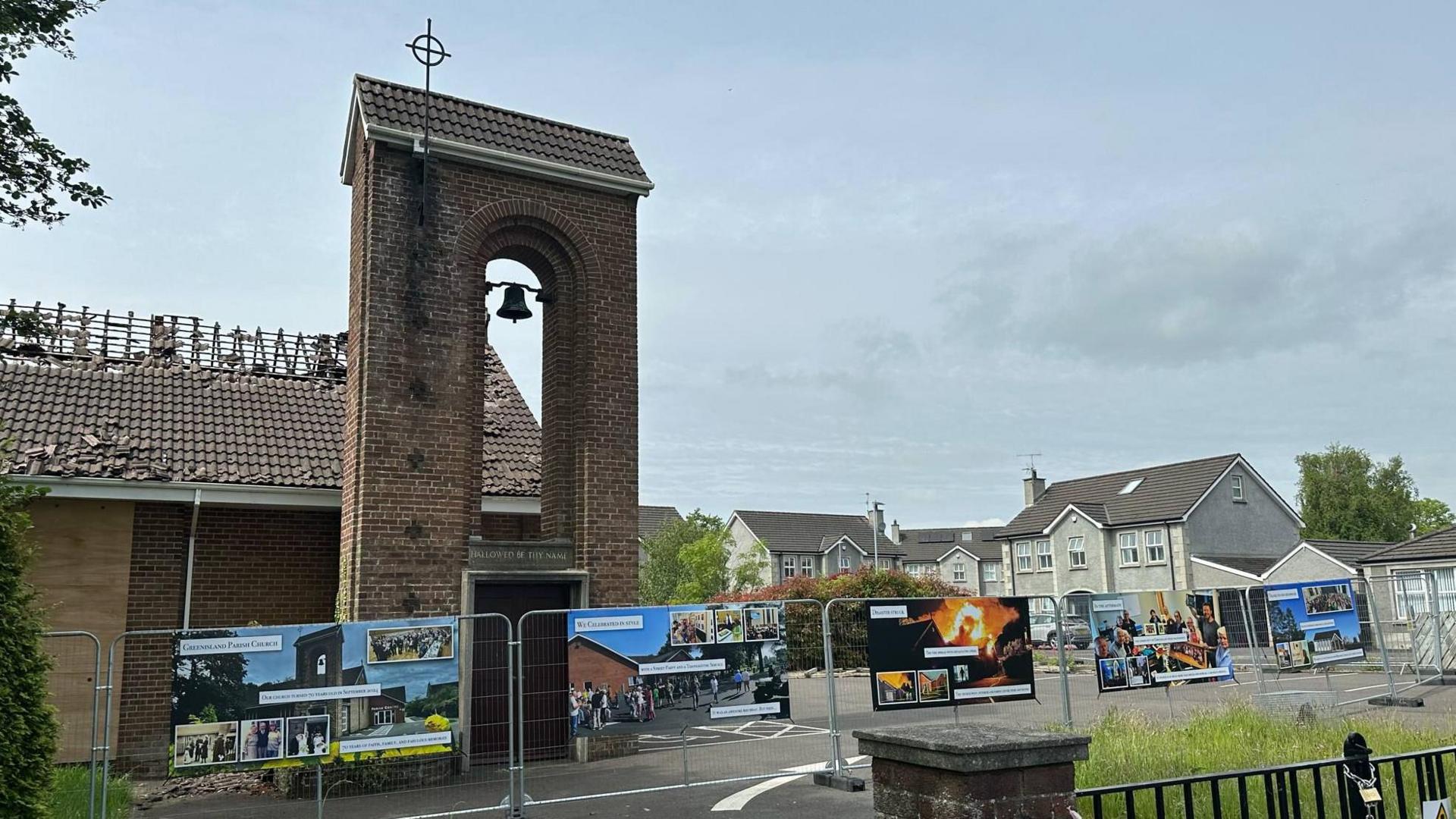 Large coloured images showing the journey of the church from the day before the fire, to the night of the fire, and the aftermath are hanging on a metal railing around the burned down church building. You can see the roof of the church building has fallen in.