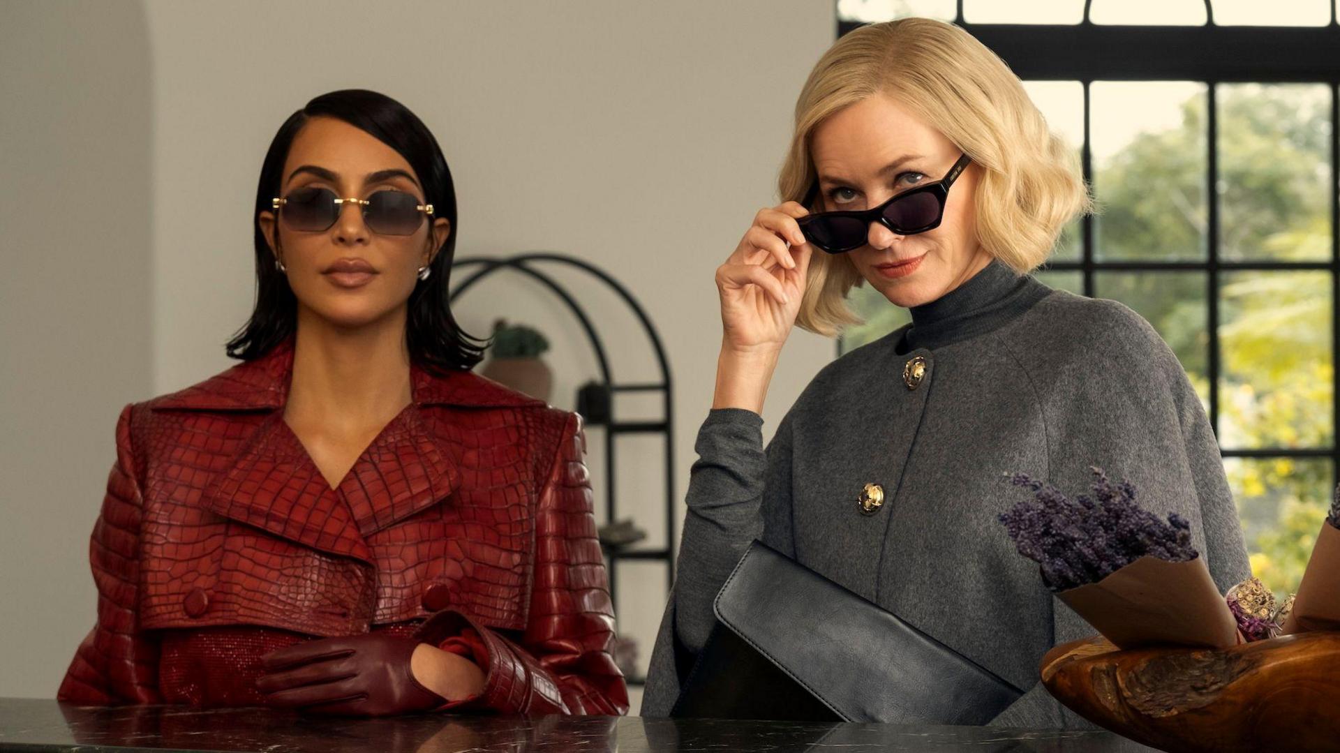 Picture of Kim Kardashian in a red coat with Naomi Watts in a grey coat. Both wear sunglasses.