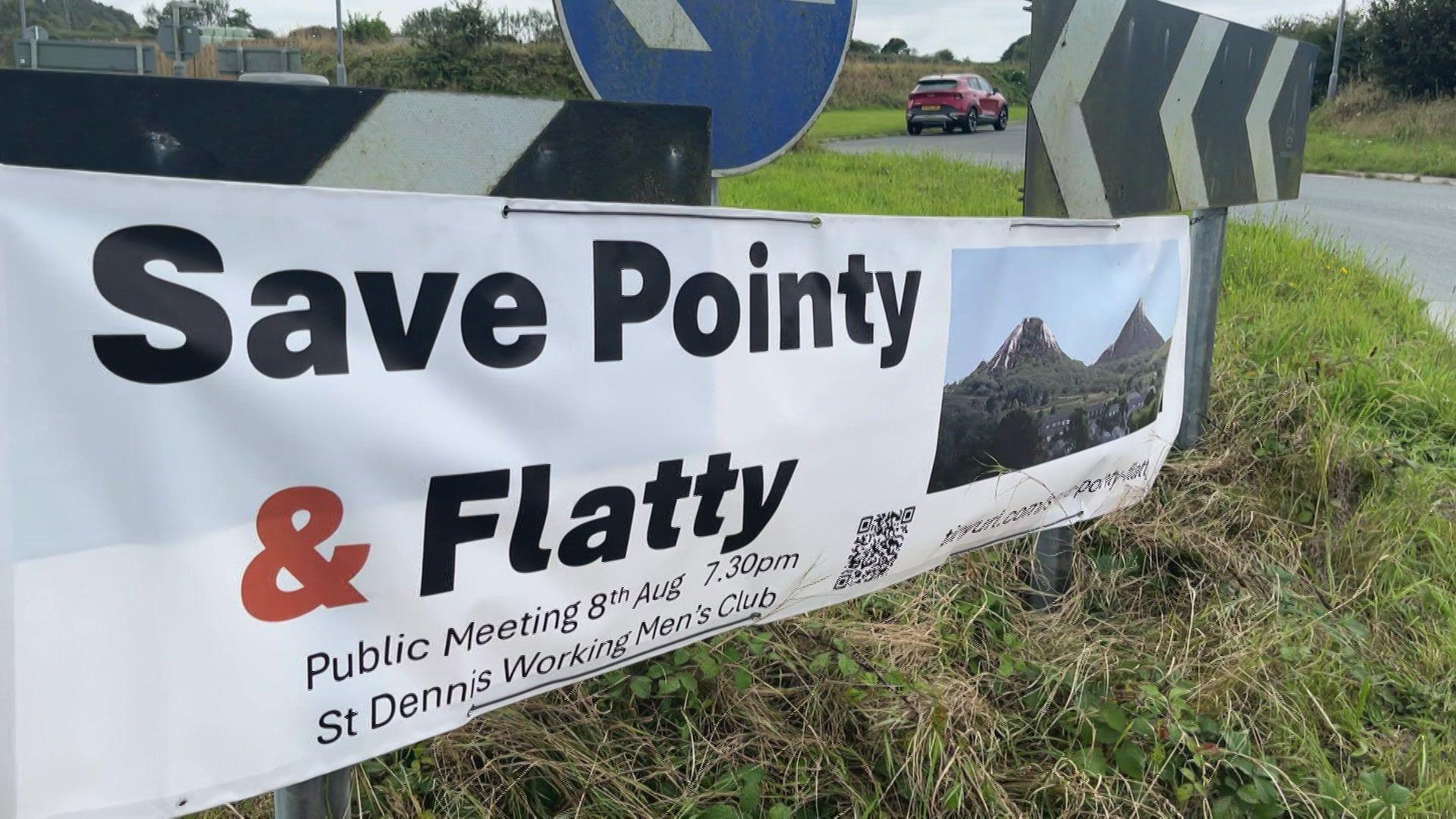 A sign reading "save pointy and flatty" put up on a roundabout. The sign features an image of the clay waste tips 