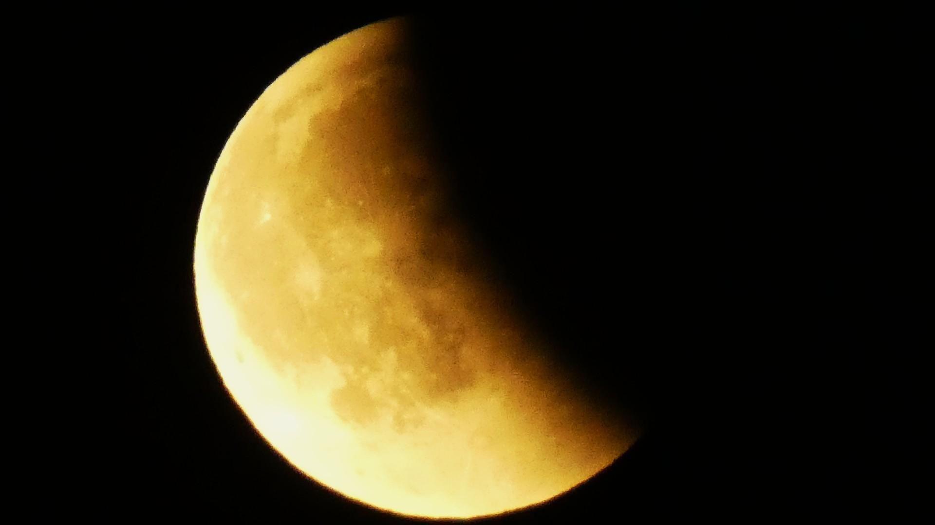 Half the Moon is covered by shadow but the rest is a dark and vibrant yellow colour