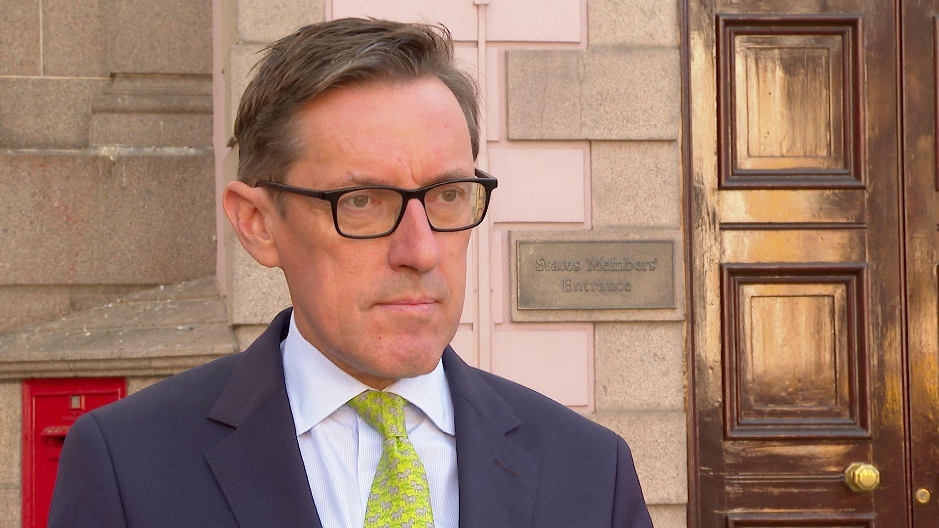 Deputy Ian Gorst outside the Jersey States building, he is wearing glasses and a yellow tie.