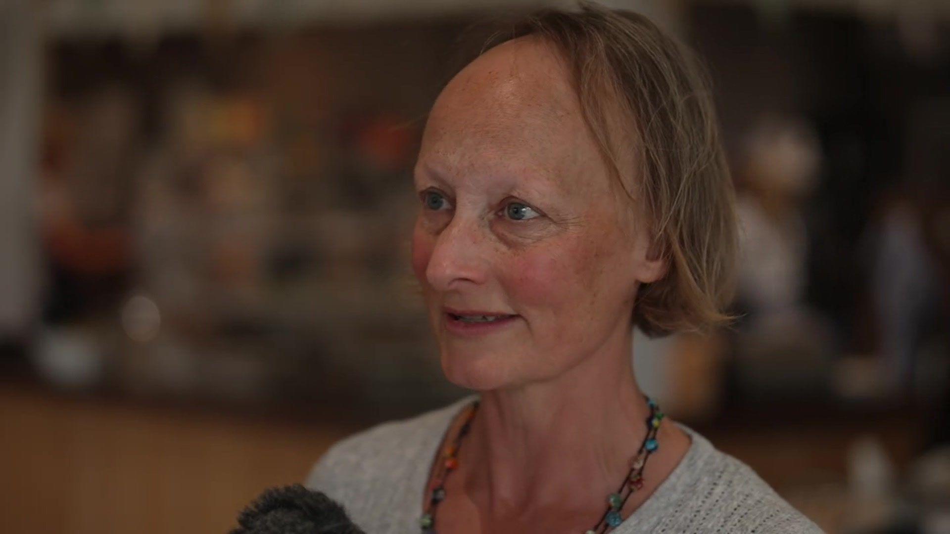 Jenny Tagney with brown hair that stop just before her shoulders. She is wearing a grey cardigan with a beaded necklace.