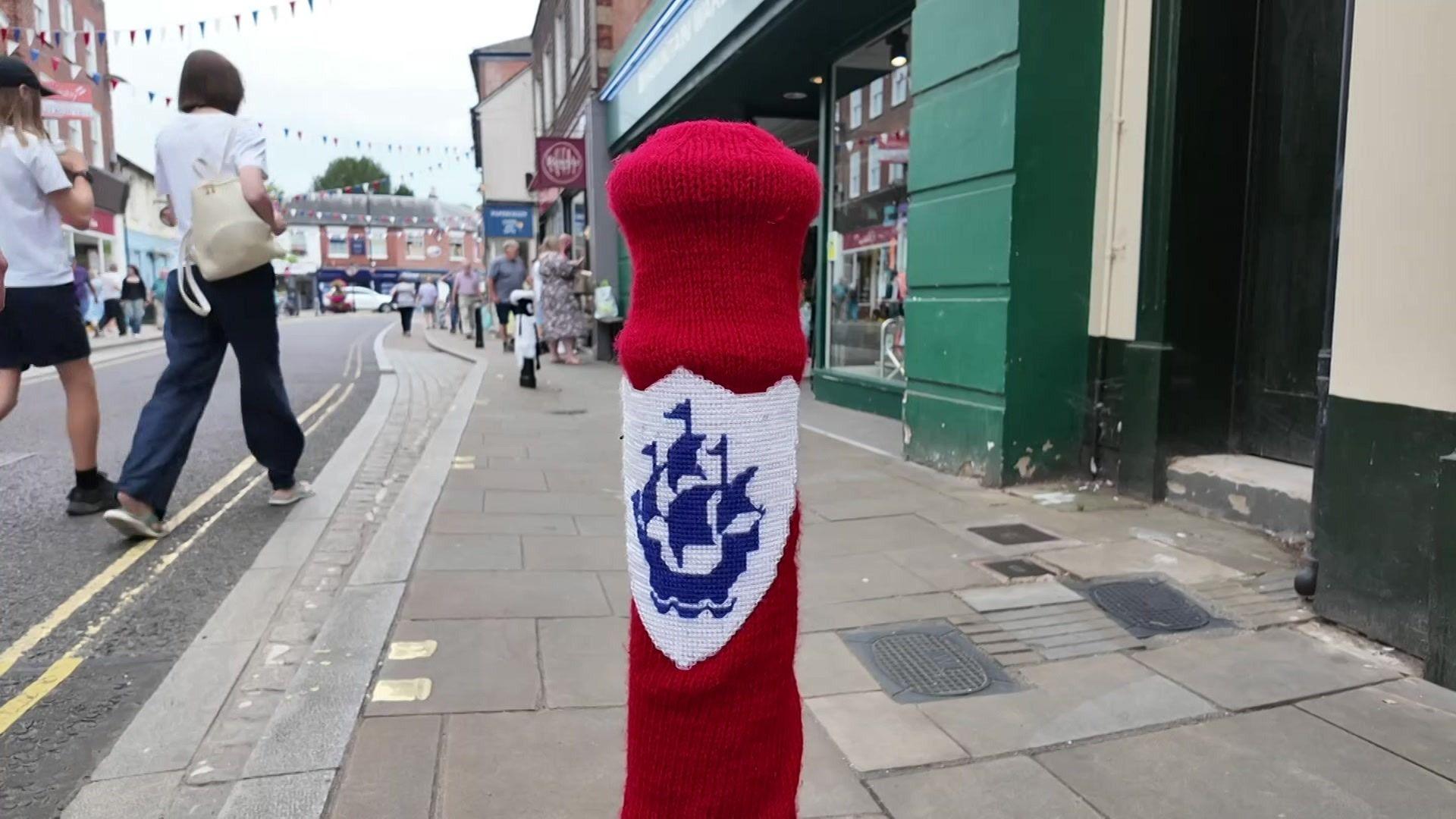 A bollard on a pavement with a Blue Peter boat logo on a red background