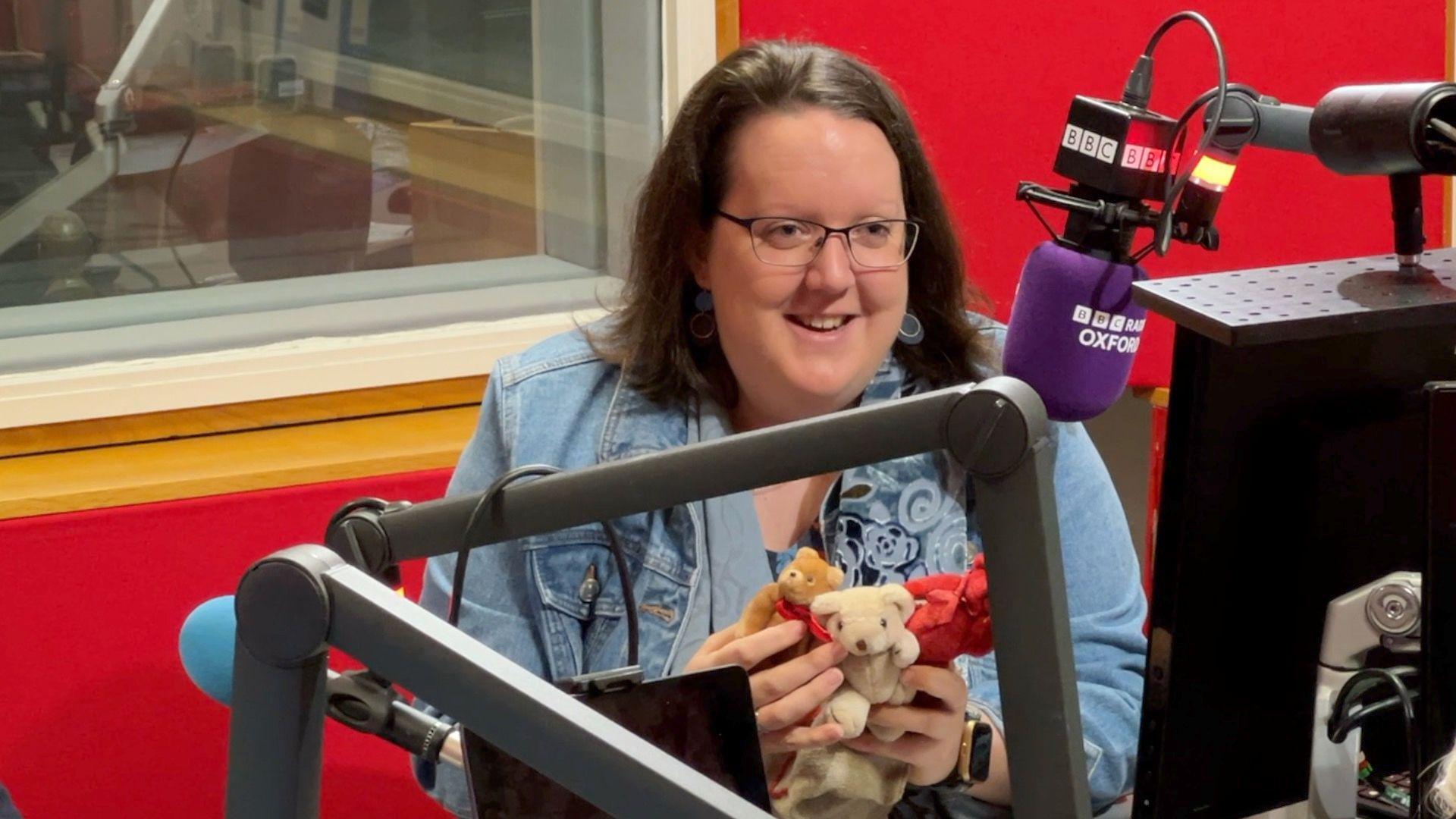 Robyn Harris in BBC Radio Oxford's studio. She holds three toy bears. She is speaking into a purple BBC branded microphone.