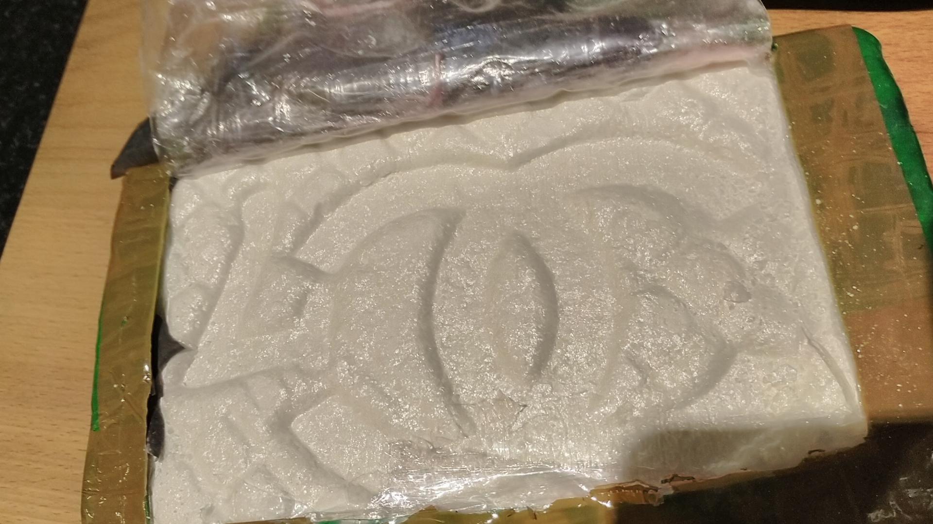 A rectangular block wrapped in masking tape, a section has been cut away on the top to reveal white powder with a Gucci style logo printed onto its surface